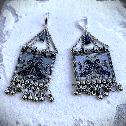 Boucles sur crochets sécurité en argent 950, composées d'un jeu de chainettes auxquelles est suspendu une plaque de métal décoré de deux paons (cloisonné et pâte de verre). J'ai suspendu des pampilles récupéré sur un vieux collier indien. jApreès avoir retiré la rouille, je les ai noirci à la peinture métal, puis brossé à la brosse acier. Elles sont protégé à la cire. Je voulais créer d'inspiration indienne avec ce couple de paon aux couleurs chatoyantes vertes, bleues et rouges