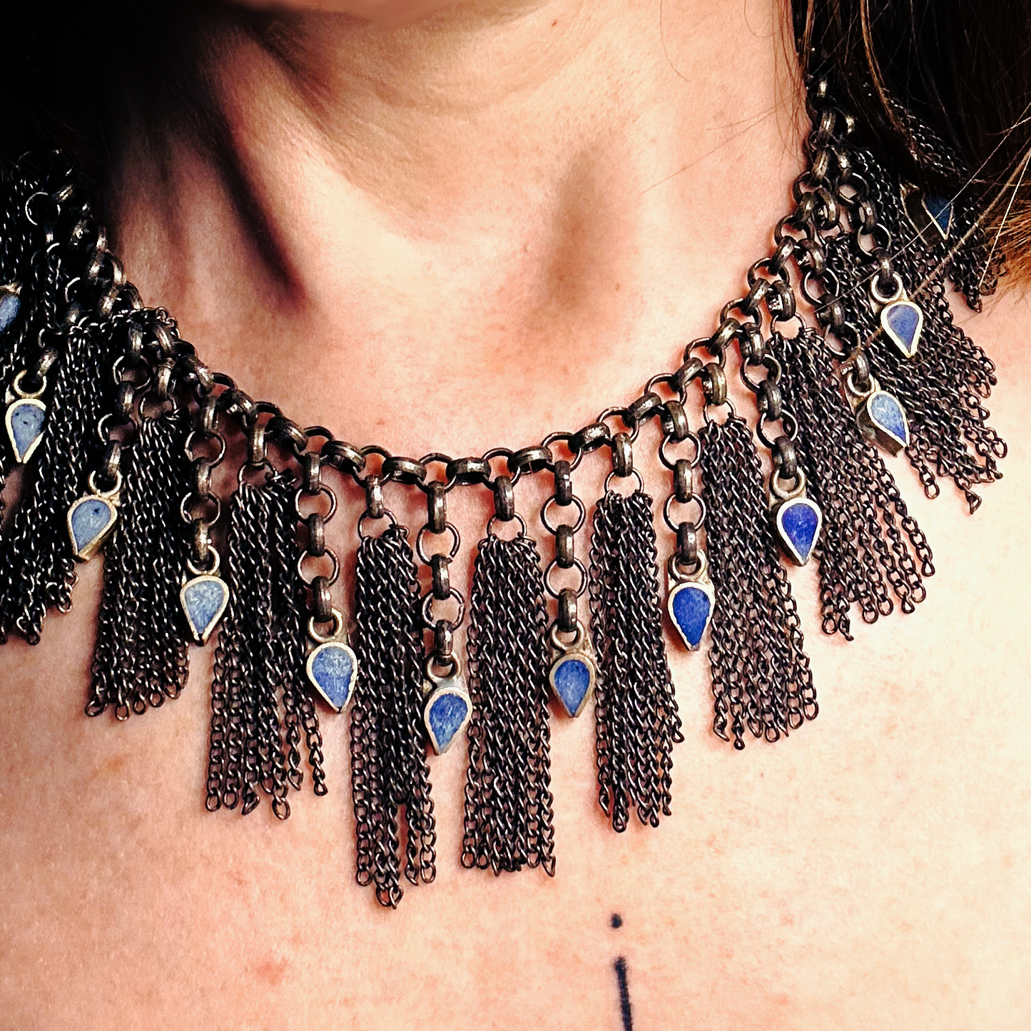 Collier en inox réalisé à de vieux maillons d'un collier cascade, de pampilles de chaines d'un collier de pampilles et de pendants en pate de verre bleu d'un vieux collier d'Essaouira. Vue portée, de près.