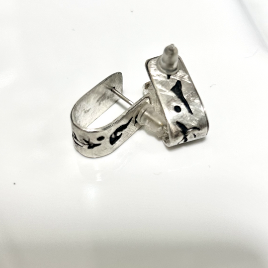 Vue de dos, boucles en argent attache par tige de part en part avec poussoir silicone, motifs de fragments éclatés du OM.