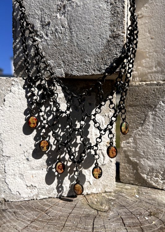 pièce unique, façonnée à partir de bijoux anciens soigneusement sélectionnés, nettoyés et réassemblés pour transmettre un message puissant:
Sept médailles religieuses vintage au fond jauni (Saints, Chérubin, Vierge), serties dans du laiton, issues d’un ancien collier de perles de culture.
Des anneaux en inox, récupérés un à un sur un collier cascade, assemblés pour créer un plastron pyramidal.