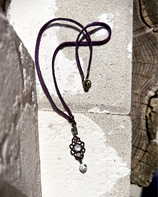 Vieux collier en suédine violette, sublimé par un charme récupéré sur un bijou ancien. J’ai ajouté deux perles : une perle japonaise en métal et une perle de verre aux tonalités délicates des cerisiers en fleurs. Tout en douceur, un brin vintage, comme un souffle léger parmi les pétales dansants des sakura. Vue posée sur une pierre.