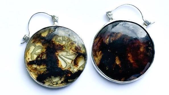 Boucles en argent de 4,5 cm de diamètre chacune, sur 6 cm de hauteur, serties de deux ambres provenant des deux veines différentes d'une mine au Chiapas, ce qui donne une particularité à cette paire de boucles harmonieuses aux couleurs variées. Le dos des sertis en argent est délicatement ajouré sur des motifs de masque illustrant le jour de la fête mexicaine Día de los Muertos, cette célébration vibrante de la vie et de la mémoire. Vues de face une ambre cleire, une ambre orangée plus sombre.