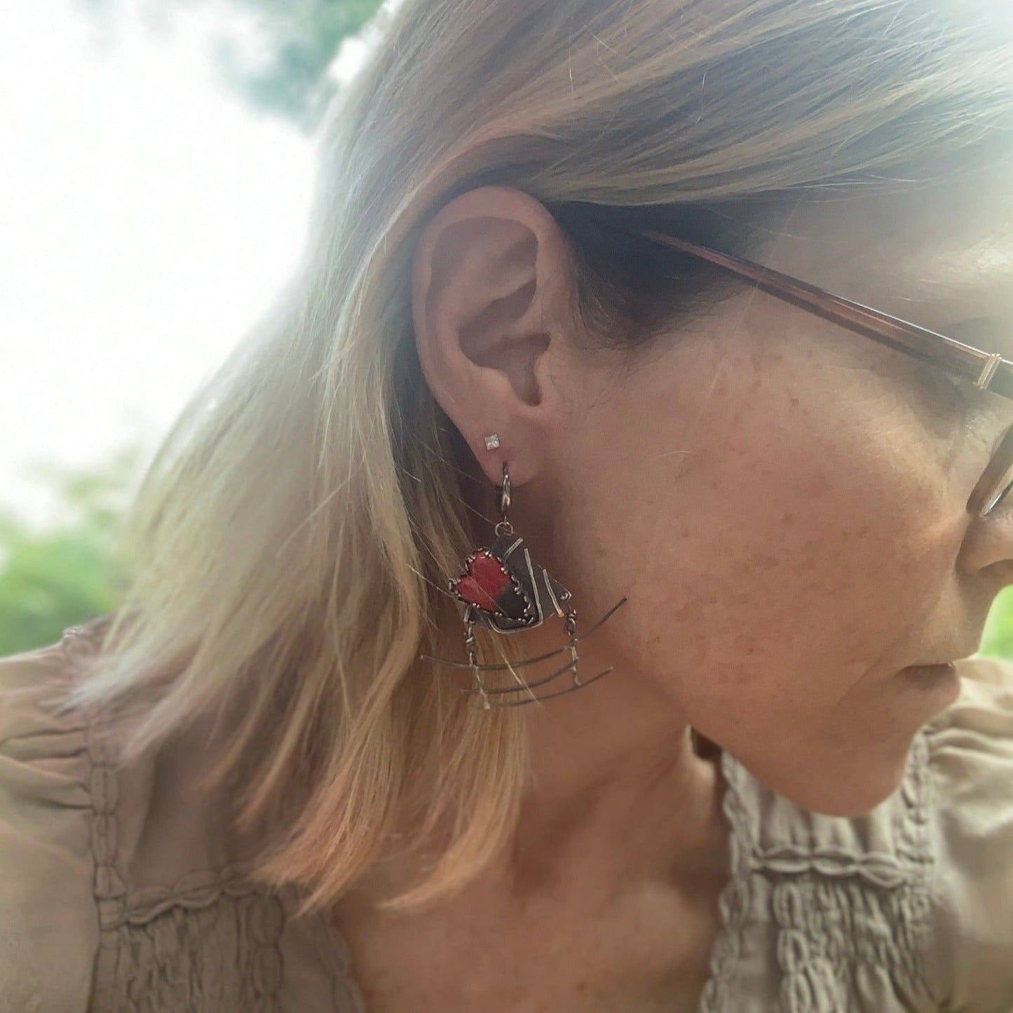 Boucles d'oreilles en argent, sur lequel est gravé l'idéogramme japonais du kokoro, qui est à la fois l'amour, l'âme, l'essence de tout. Par dessus sur une plateforme est serti un cœur en céramique raku. Sous cette partie haute de boucles d'oreilles est suspendue le symbole du Torii. Le tout est entièrement forgé en argent 950. Vue de face.