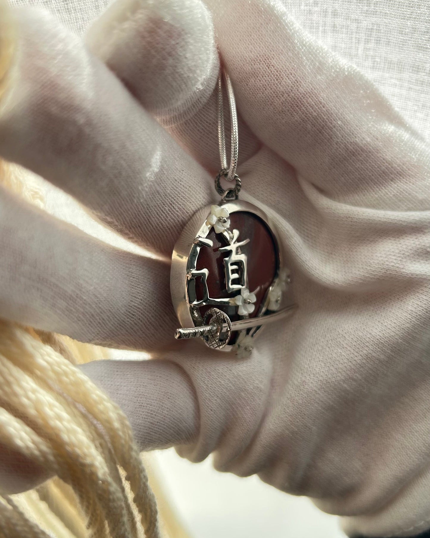 pendentif en argent portant le Do du chemin, le sabre de l'iaido et les fleurs de sakura en nacre. Vue de 3/4 côté gauche côté rondelle, avec sabre en relief et fleurs en nacre rivetées
