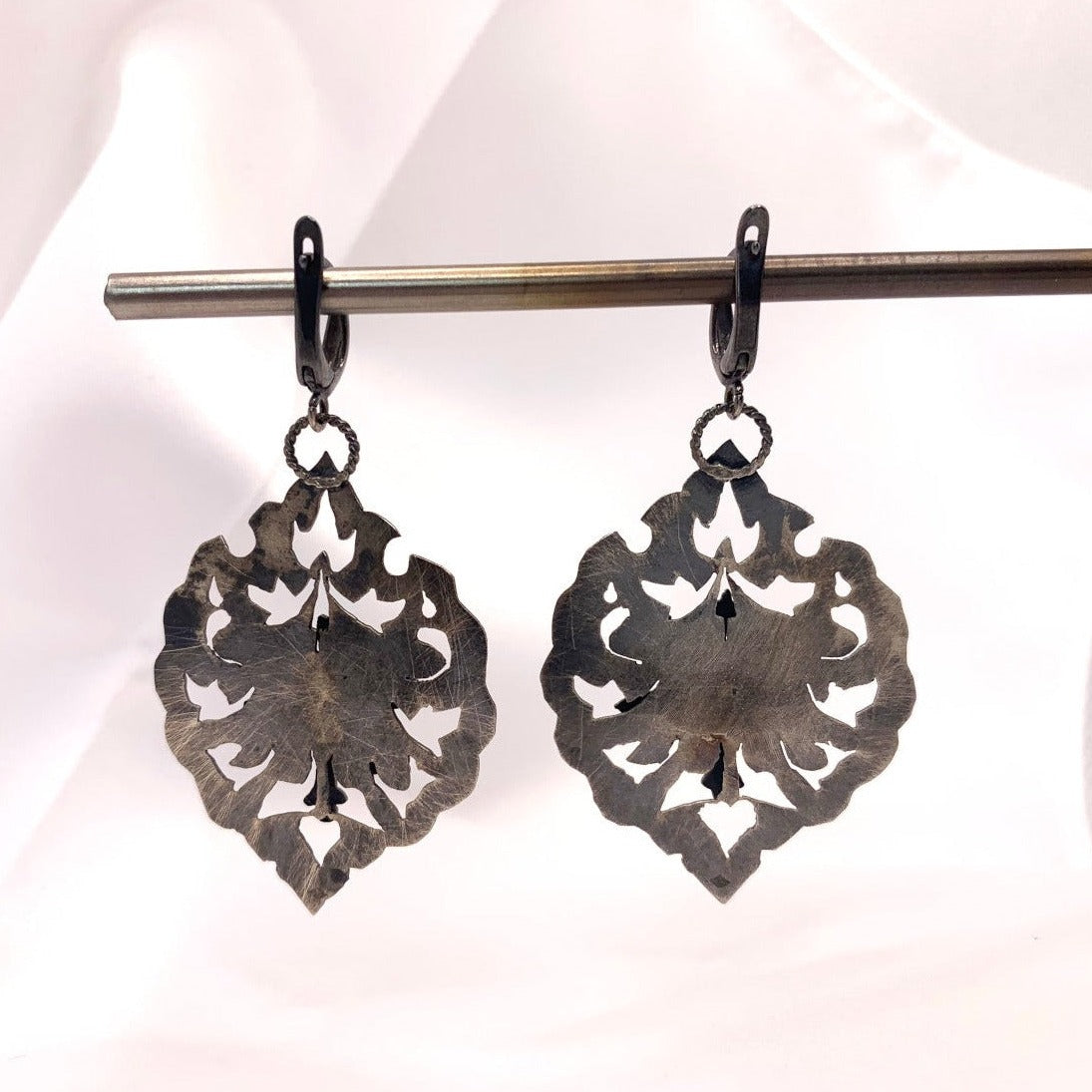 Ces boucles en argent sont constituées de deux plaques superposées et soudées avec un écart afin que la fleur centrale soit surélevée. Au creux de cette fleur repose un serti e vésuvianite d'un vert éclatant. Inspiré des motifs hatayi. vue de dos soit la fleur principale lisse et brossée à la laine d'acier et oxydé. Crochets d'oreille à clips en argent.