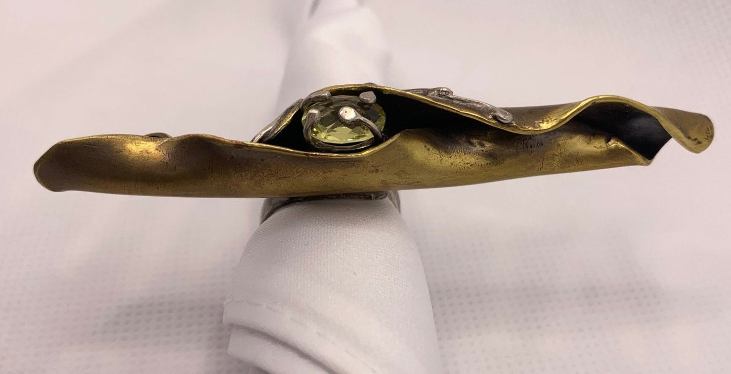 Bague en laiton forgé comme une feuille d'arbuste enroulée par le vent, elle couvre 4 doigts, repose sur un jonc réglable en laiton. En son cœur repose un serti en argent avec un quartz jaune facetté. Vue macro opposée.