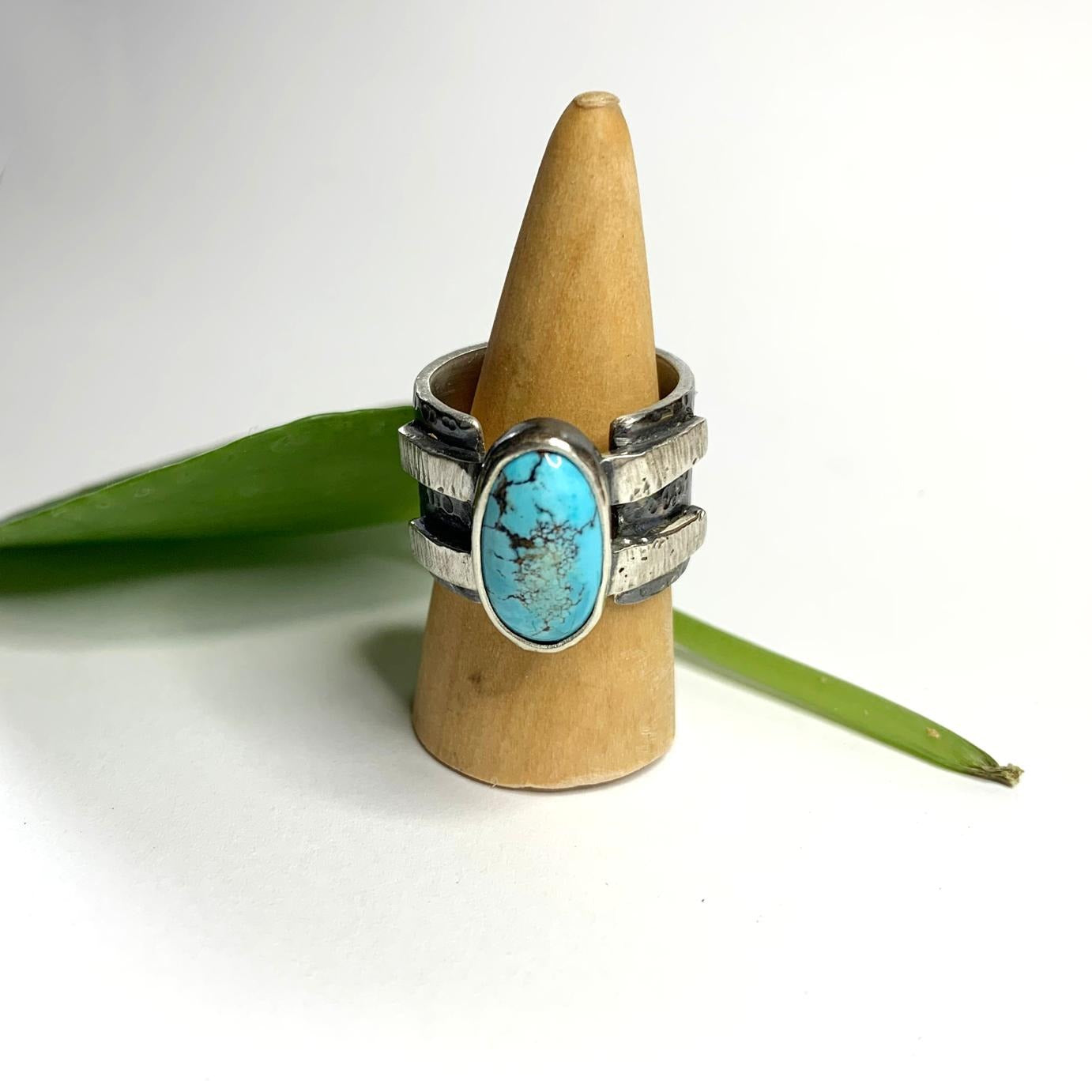 Bague en argent épaisse et martelée, inspirée du design des bracelets de force, sertie d'une turquoise d'Iran. Le serti repose sur deux bandes d'argent soudées, intégrées dans la continuité du jonc, assurant ainsi sa fermeture. Taille 59, vue de face.