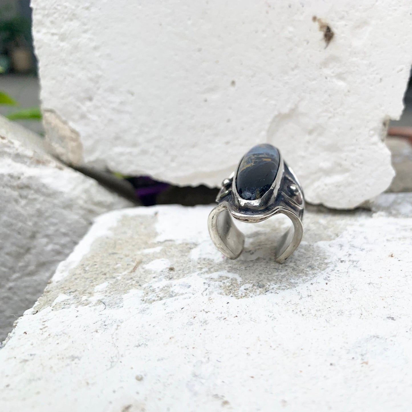 Bague réglable en argent avec un large aplat sur le dessus serti d'une pietersite bleu nuit, entourée de deux symboles de demi-lune berbère texturé. Chaque demi-lune de part et d'autres de la pierre possède une bille centrale qui vient compléter ce symbole porte bonheur. Argent oxydé tons bleus. Vue de coupe.