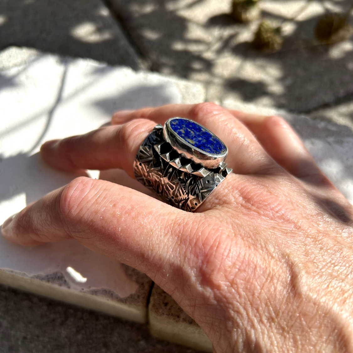 bague en argent, jonc gravé de symboles fait par poiçonnage, surplombé d'un plateforme de barre de triangles smbolisant un bûcher, sertie d'un lapis lazuli symbolisant le ciel étoilé. Mksha car elle symbolise l'inhumation indienne d'un proche chéri au moment ou l'âme se détache du corps pour atteindre le nirvana, la moksha.