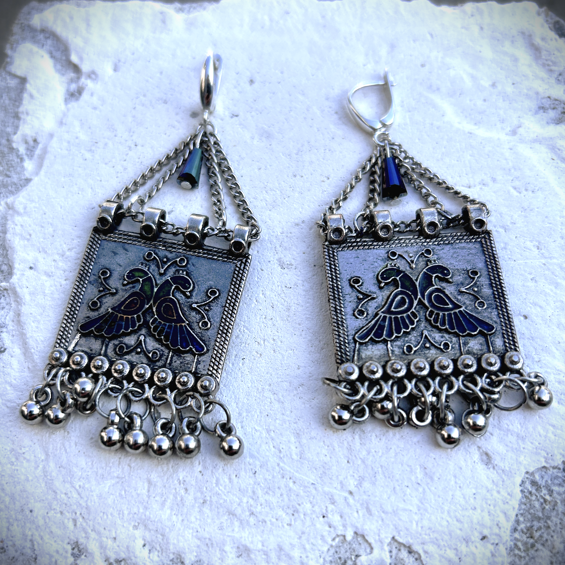 Boucles sur crochets sécurité en argent 950, composées d'un jeu de chainettes auxquelles  est suspendu une plaque de métal décoré de deux paons (cloisonné et pâte de verre). J'ai suspendu des pampilles récupéré sur un vieux collier indien.  jApreès avoir retiré la rouille, je les ai noirci à la peinture métal, puis brossé à la brosse acier. Elles sont protégé à la cire. Je voulais  créer d'inspiration indienne avec ce couple de paon aux couleurs chatoyantes vertes, bleues et rouges