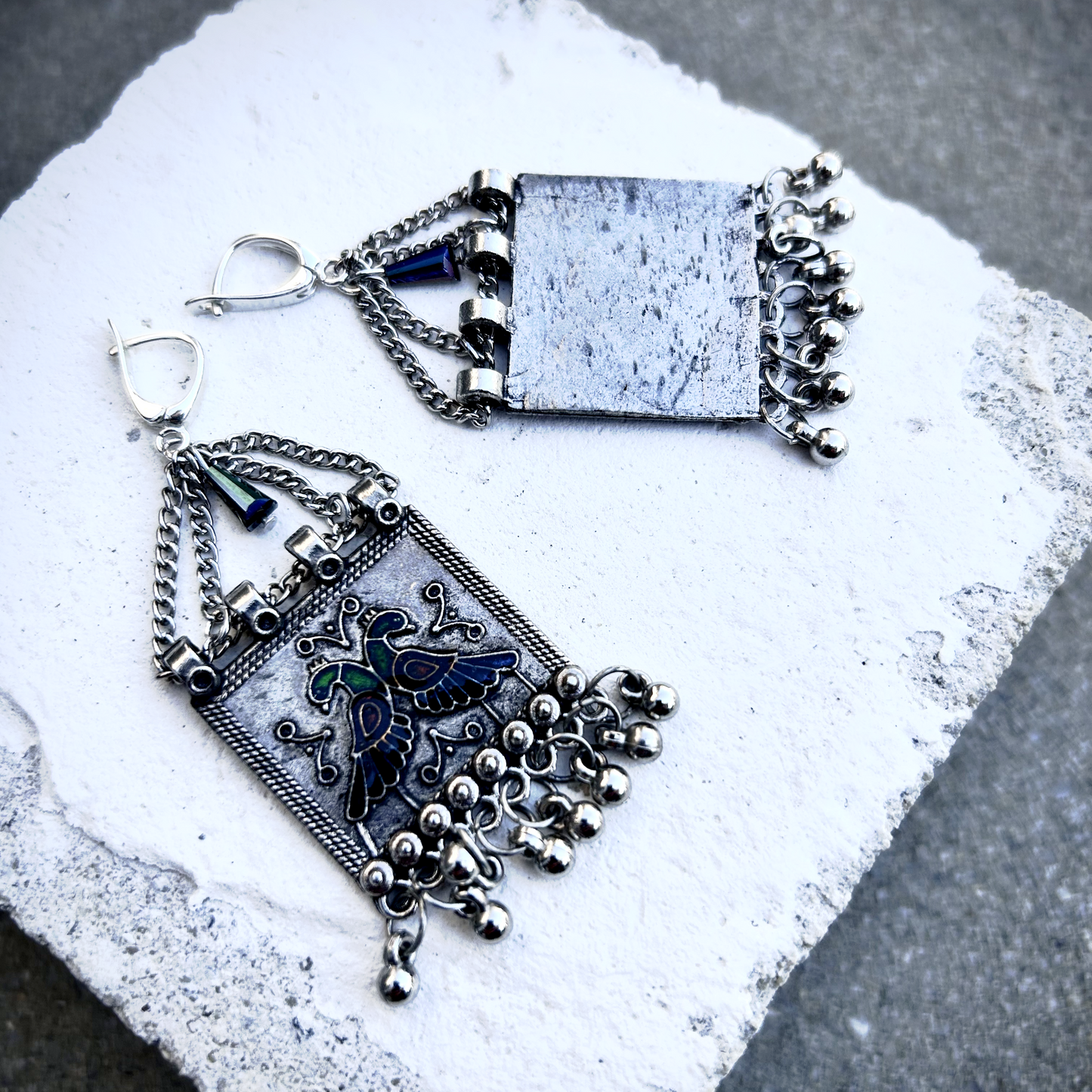 Boucles sur crochets sécurité en argent 950, composées d'un jeu de chainettes auxquelles  est suspendu une plaque de métal décoré de deux paons (cloisonné et pâte de verre). J'ai suspendu des pampilles récupéré sur un vieux collier indien.  jApreès avoir retiré la rouille, je les ai noirci à la peinture métal, puis brossé à la brosse acier. Elles sont protégé à la cire. Je voulais  créer d'inspiration indienne avec ce couple de paon aux couleurs chatoyantes vertes, bleues et rouges. Vues face / dos.