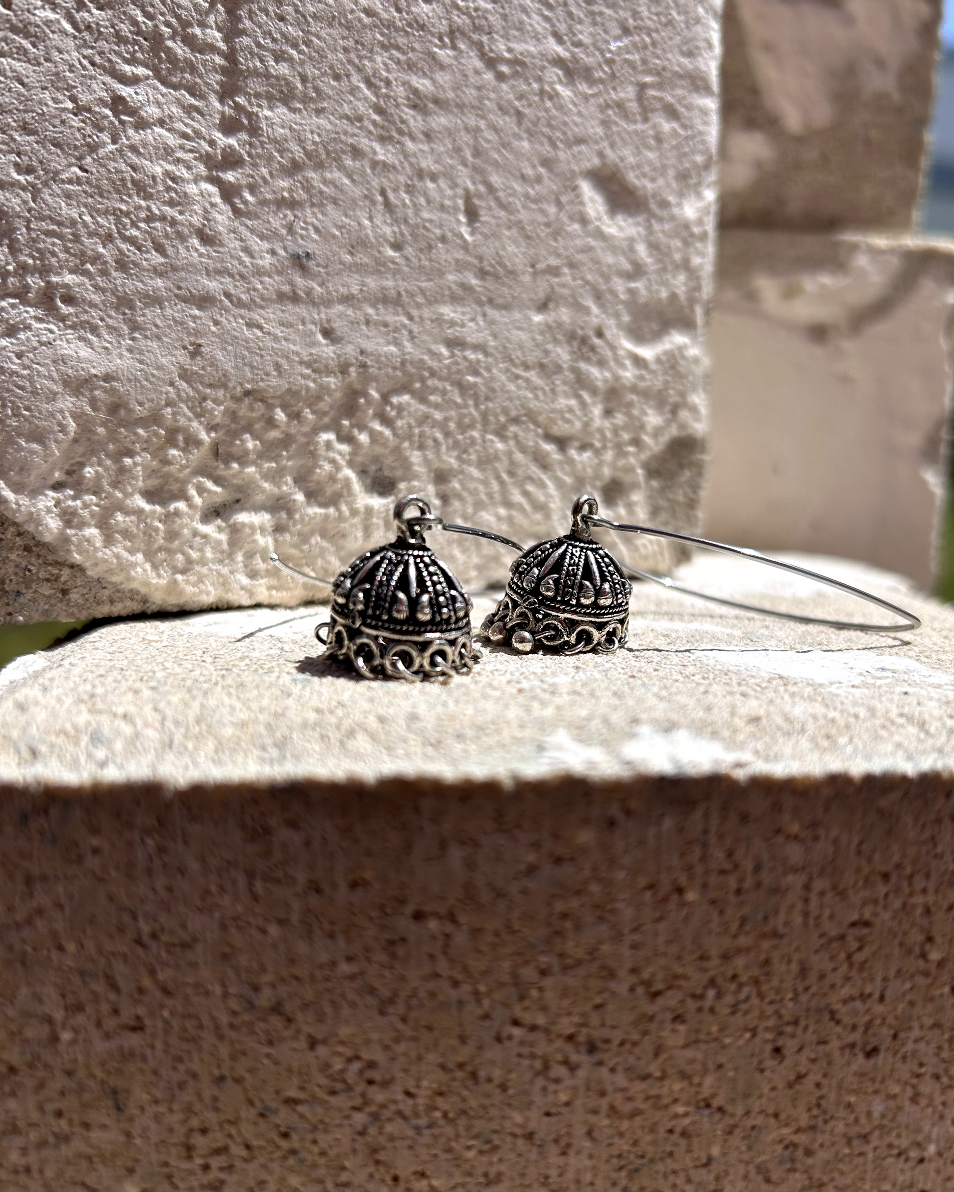 Deux boucles d’une simplicité absolue, réalisées à partir d’un crochet en inox en V, sur lequel j’ai suspendu un charme récupéré d’une paire de boucles d’oreilles indiennes de mariage. J’ai recomposé certaines pampilles disparues grâce à des tiges en acier inoxydable. Un équilibre parfait entre douceur et un parfum d’ailleurs. Vue posées sur une pierre 