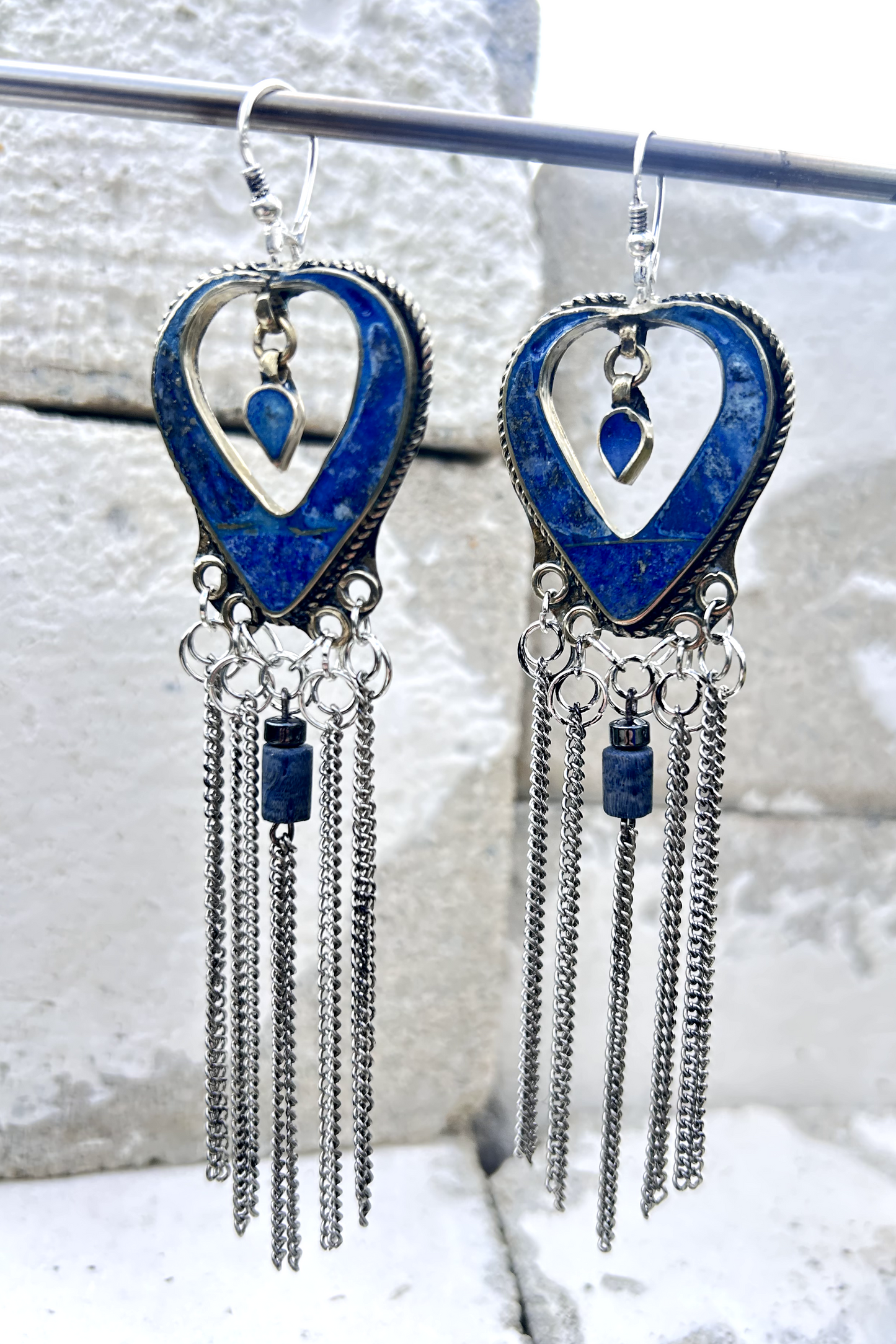 Boucles d'oreilles longues réalisées à partir de deux pendentif coeur d'un vieux collier d'Essaouira, sciées, limées, émerisé, polies et entièrement vernies, y comris la pate de verre bleu sertie dans le cloisonné. Dessous j'ai gardé qelques attaches pour construire un jeu d'anneau en inox auxquels j'ai supsendu des chaines et deux perles (une hématite, et une perle en pierre bleue). Au centre du coeur j'ai suspendu un petit charme du colllier pour illustrer les larmes du coeur. Vue de face.