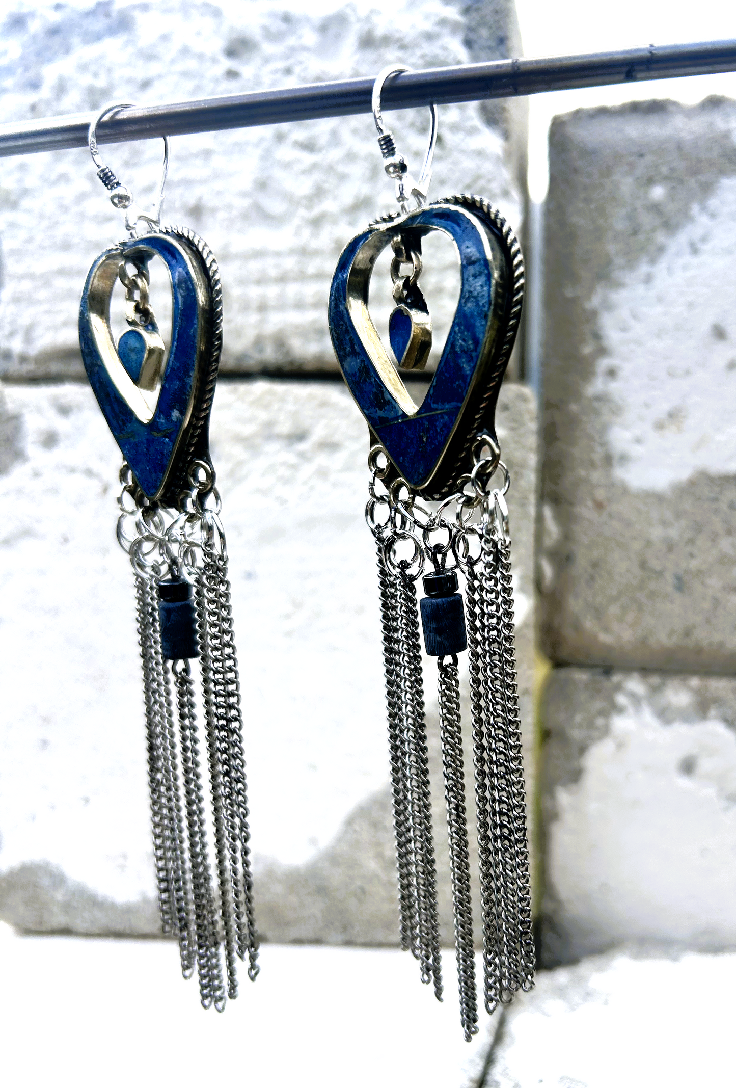 Boucles d'oreilles longues réalisées à partir de deux pendentif coeur d'un vieux collier d'Essaouira, sciées, limées, émerisé, polies et entièrement vernies, y comris la pate de verre bleu sertie dans le cloisonné. Dessous j'ai gardé qelques attaches pour construire un jeu d'anneau en inox auxquels j'ai supsendu des chaines et deux perles (une hématite, et une perle en pierre bleue). Au centre du coeur j'ai suspendu un petit charme du colllier pour illustrer les larmes du coeur. Vue de profil.