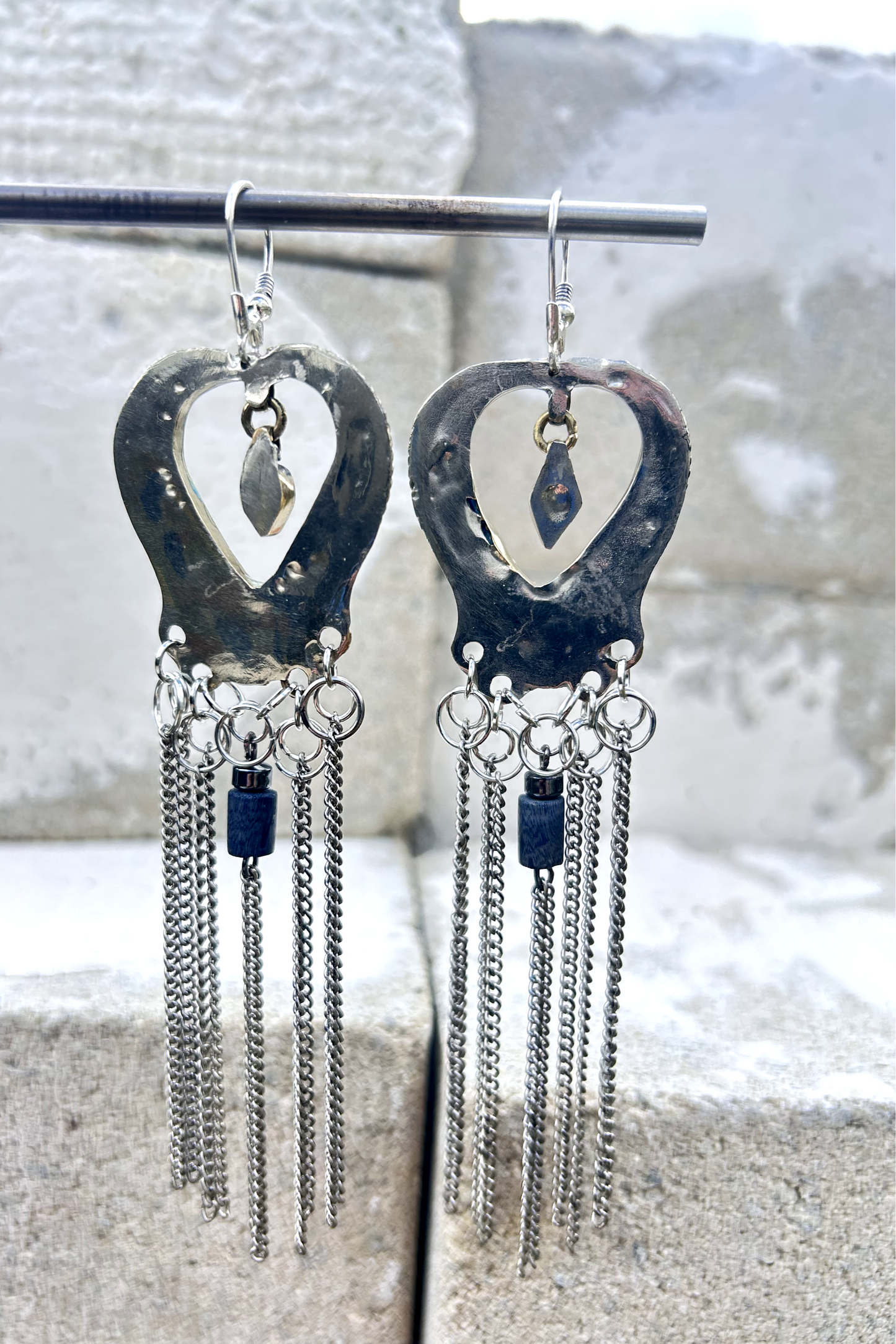 Boucles d'oreilles longues réalisées à partir de deux pendentif coeur d'un vieux collier d'Essaouira, sciées, limées, émerisé, polies et entièrement vernies, y comris la pate de verre bleu sertie dans le cloisonné. Dessous j'ai gardé qelques attaches pour construire un jeu d'anneau en inox auxquels j'ai supsendu des chaines et deux perles (une hématite, et une perle en pierre bleue). Au centre du coeur j'ai suspendu un petit charme du colllier pour illustrer les larmes du coeur. Vue de dos, vernis.