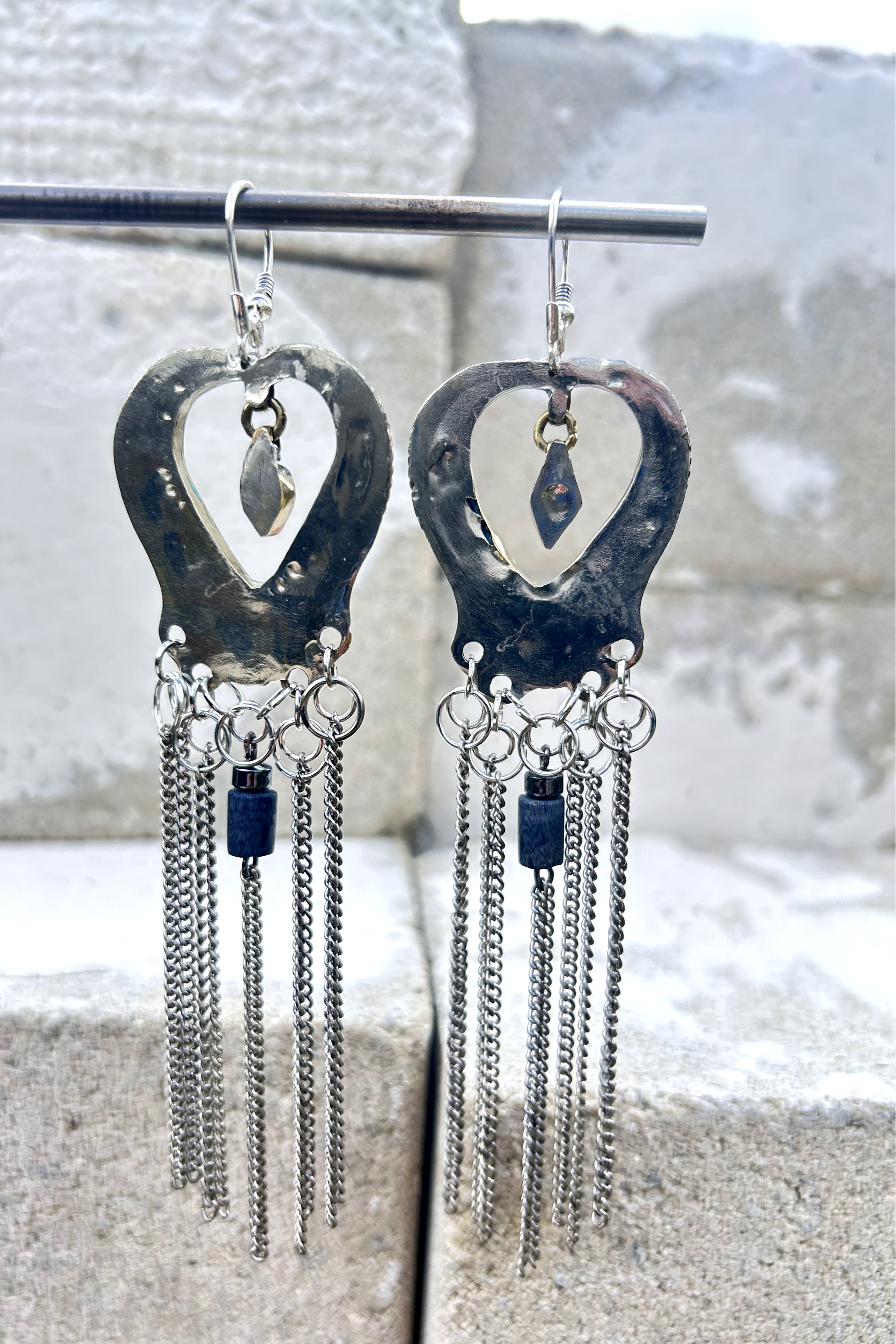 Boucles d'oreilles longues réalisées à partir de deux pendentif coeur d'un vieux collier d'Essaouira, sciées, limées, émerisé, polies et entièrement vernies, y comris la pate de verre bleu sertie dans le cloisonné. Dessous j'ai gardé qelques attaches pour construire un jeu d'anneau en inox auxquels j'ai supsendu des chaines et deux perles (une hématite, et une perle en pierre bleue). Au centre du coeur j'ai suspendu un petit charme du colllier pour illustrer les larmes du coeur. Vue de dos, vernis.