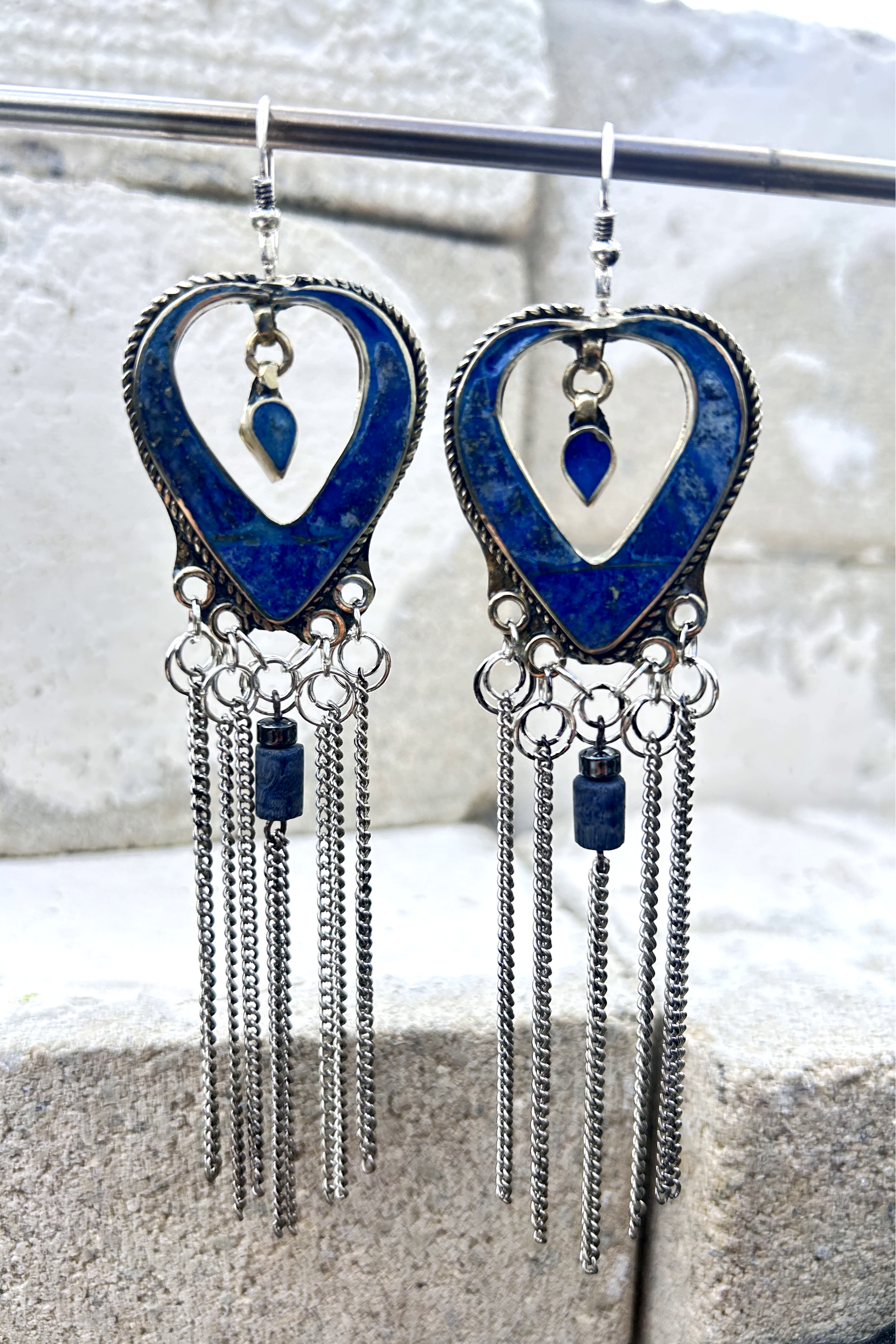 Boucles d'oreilles longues réalisées à partir de deux pendentif coeur d'un vieux collier d'Essaouira, sciées, limées, émerisé, polies et entièrement vernies, y comris la pate de verre bleu sertie dans le cloisonné. Dessous j'ai gardé qelques attaches pour construire un jeu d'anneau en inox auxquels j'ai supsendu des chaines et deux perles (une hématite, et une perle en pierre bleue). Au centre du coeur j'ai suspendu un petit charme du colllier pour illustrer les larmes du coeur. Vue de face.