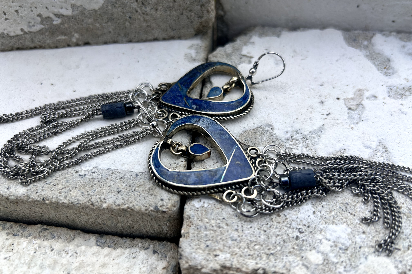 Boucles d'oreilles longues réalisées à partir de deux pendentif coeur d'un vieux collier d'Essaouira, sciées, limées, émerisé, polies et entièrement vernies, y comris la pate de verre bleu sertie dans le cloisonné. Dessous j'ai gardé qelques attaches pour construire un jeu d'anneau en inox auxquels j'ai supsendu des chaines et deux perles (une hématite, et une perle en pierre bleue). Au centre du coeur j'ai suspendu un petit charme du colllier pour illustrer les larmes du coeur. Vue de dessus