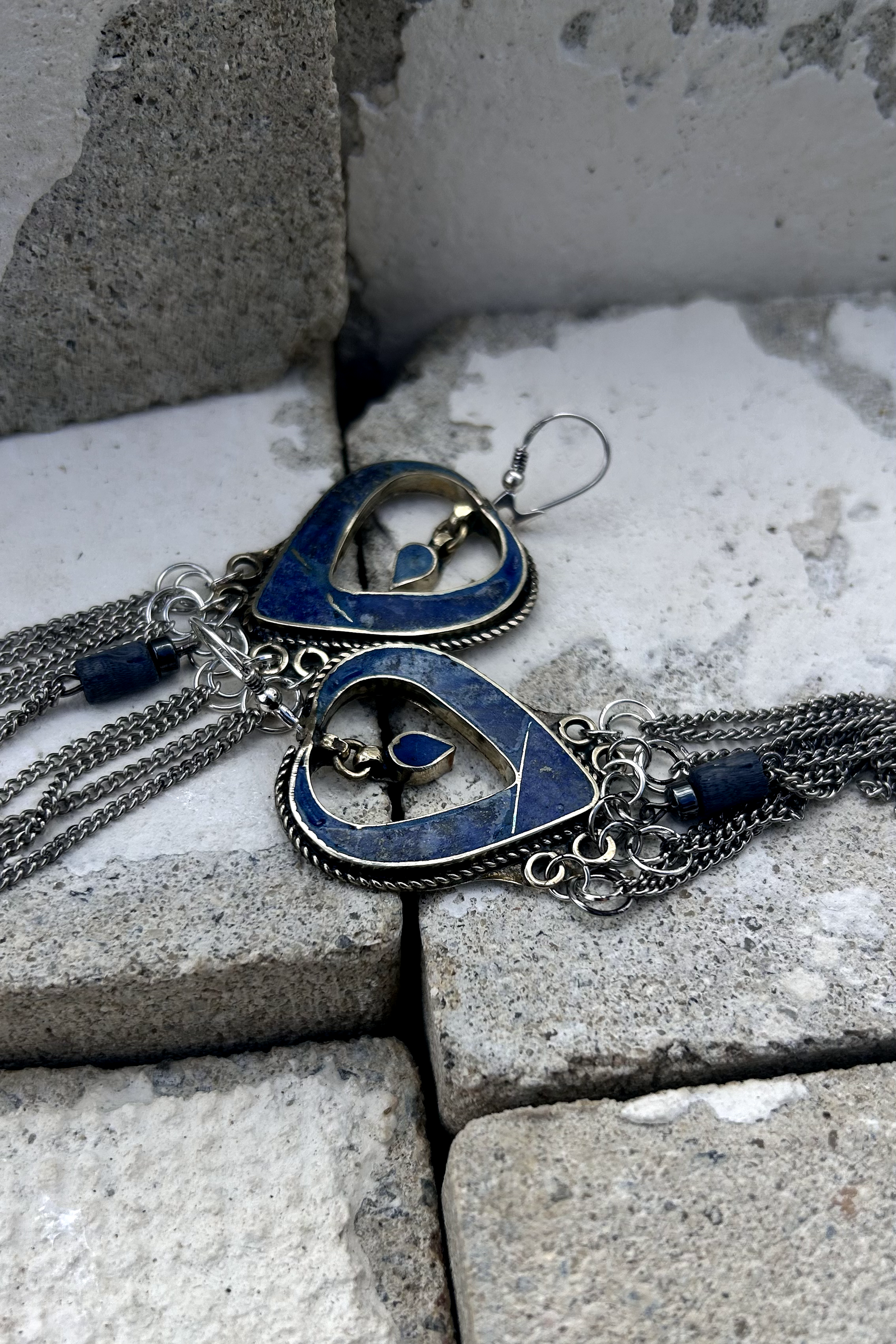 Boucles d'oreilles longues réalisées à partir de deux pendentif coeur d'un vieux collier d'Essaouira, sciées, limées, émerisé, polies et entièrement vernies, y comris la pate de verre bleu sertie dans le cloisonné. Dessous j'ai gardé qelques attaches pour construire un jeu d'anneau en inox auxquels j'ai supsendu des chaines et deux perles (une hématite, et une perle en pierre bleue). Au centre du coeur j'ai suspendu un petit charme du colllier pour illustrer les larmes du coeur. Vue de profil.