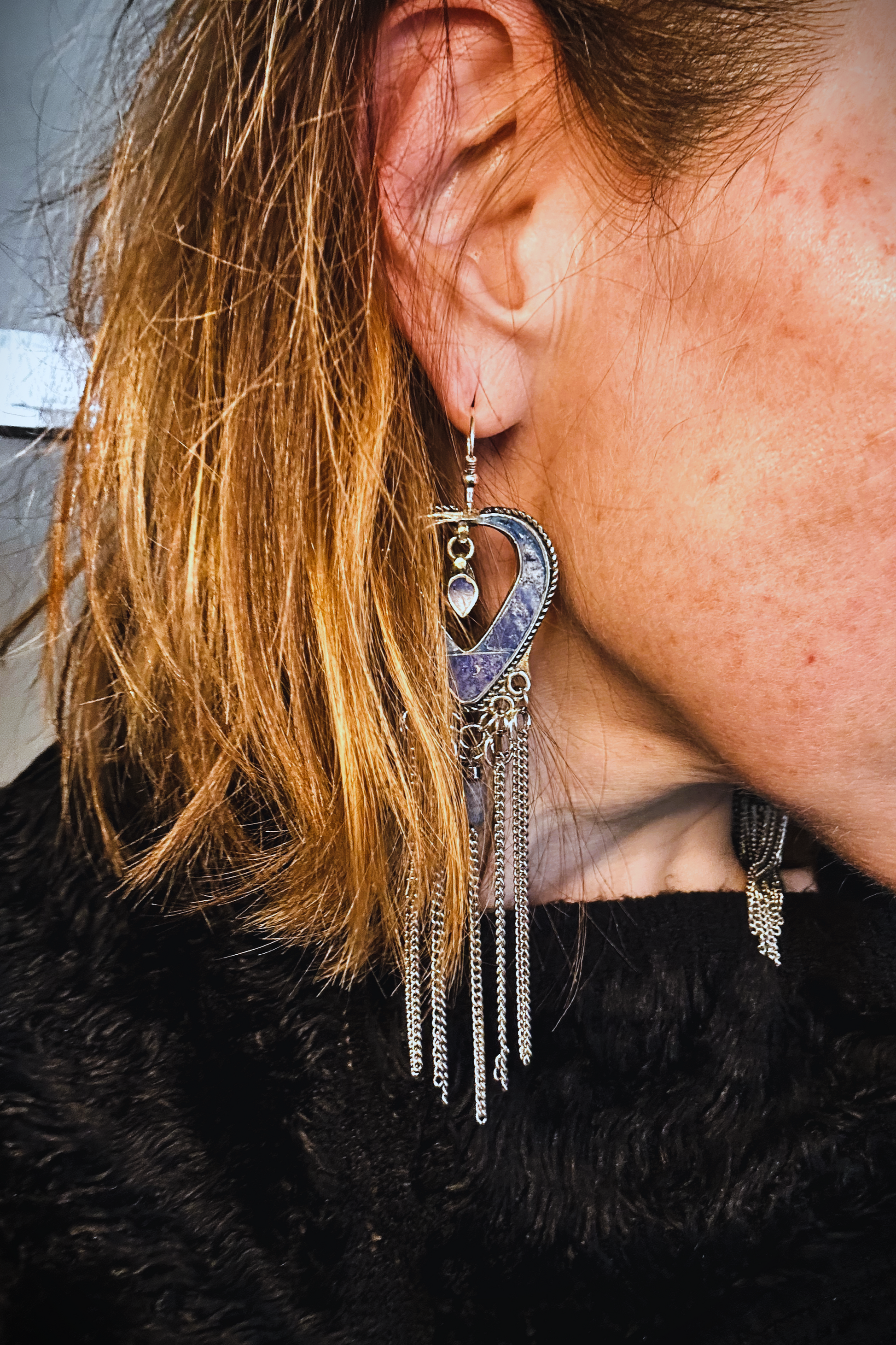 Boucles d'oreilles longues réalisées à partir de deux pendentif coeur d'un vieux collier d'Essaouira, sciées, limées, émerisé, polies et entièrement vernies, y comris la pate de verre bleu sertie dans le cloisonné. Dessous j'ai gardé qelques attaches pour construire un jeu d'anneau en inox auxquels j'ai supsendu des chaines et deux perles (une hématite, et une perle en pierre bleue). Au centre du coeur j'ai suspendu un petit charme du colllier pour illustrer les larmes du coeur. Vue portée.