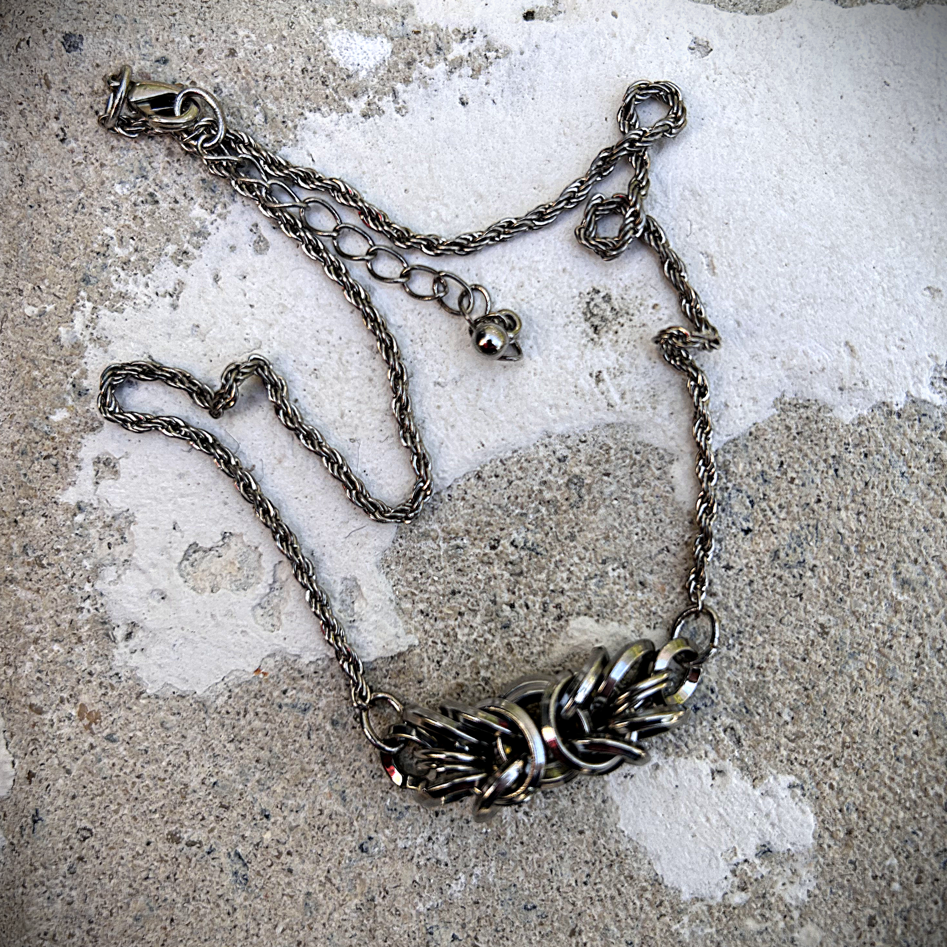 Ce collier ras-de-cou est composé d'une chaîne torsadée en acier inoxydable, récupérée sur un collier vintage avec médaillon central, au centre de laquelle j'ai intégré trois centimètres de maille byzantine.

J'ai soigneusement assemblé et structuré cette maille, appelée byzantine, à partir d'anneaux en acier inoxydable 304 (8 × 1,8 mm et 10 × 1,8 mm), préformés et sélectionnés pour leur solidité et leur finition biseautée.