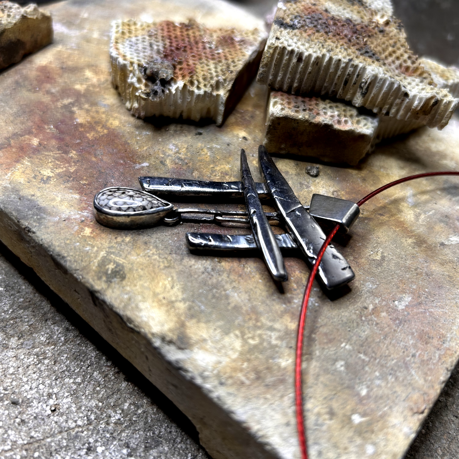 gros plan sur pendentif réalisé à partir de débris d'argent assemblés et compressés, sculptés en Torii -portail japonais d'accès au monde des esprits. Au centre de a porte est suspendu une pierre de fossile serpent sertie.