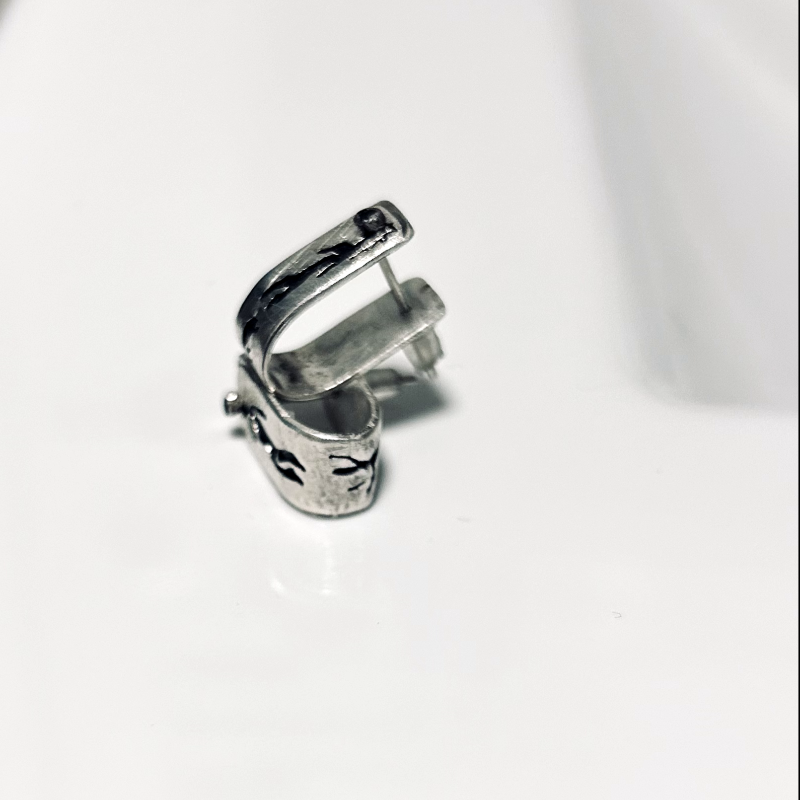 Vue de profil, boucles en argent forme agrafes, texturées, patinéss, oxydées, symboles rupestres homme et sa compagne enceinte et fragments éclatés du OM.