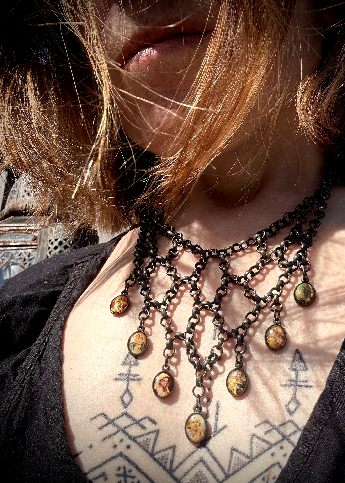 pièce unique, façonnée à partir de bijoux anciens soigneusement sélectionnés, nettoyés et réassemblés pour transmettre un message puissant:

Sept médailles religieuses vintage au fond jauni (Saints, Chérubin, Vierge), serties dans du laiton, issues d’un ancien collier de perles de culture.
Des anneaux en inox, récupérés un à un sur un collier cascade, assemblés pour créer un plastron pyramidal. Vue porté.