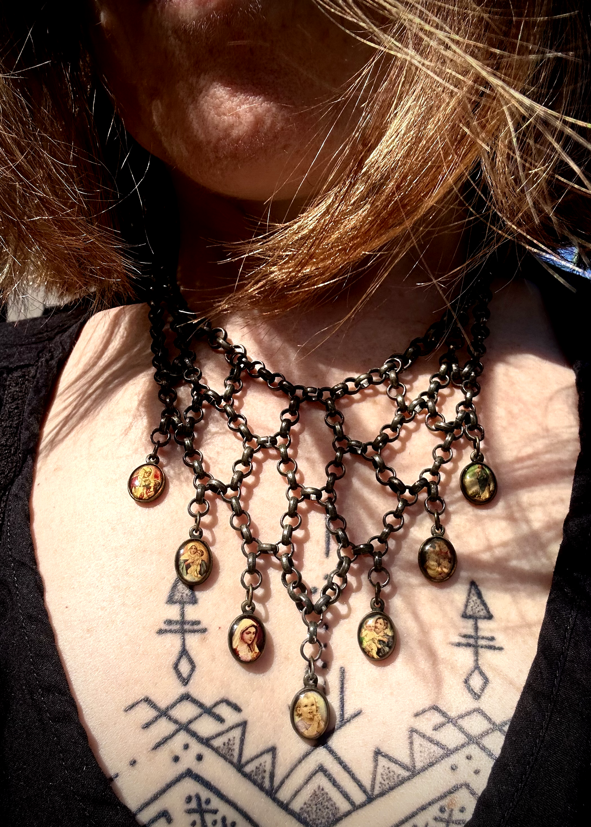 pièce unique, façonnée à partir de bijoux anciens soigneusement sélectionnés, nettoyés et réassemblés pour transmettre un message puissant:

Sept médailles religieuses vintage au fond jauni (Saints, Chérubin, Vierge), serties dans du laiton, issues d’un ancien collier de perles de culture.
Des anneaux en inox, récupérés un à un sur un collier cascade, assemblés pour créer un plastron pyramidal. Vue portée.