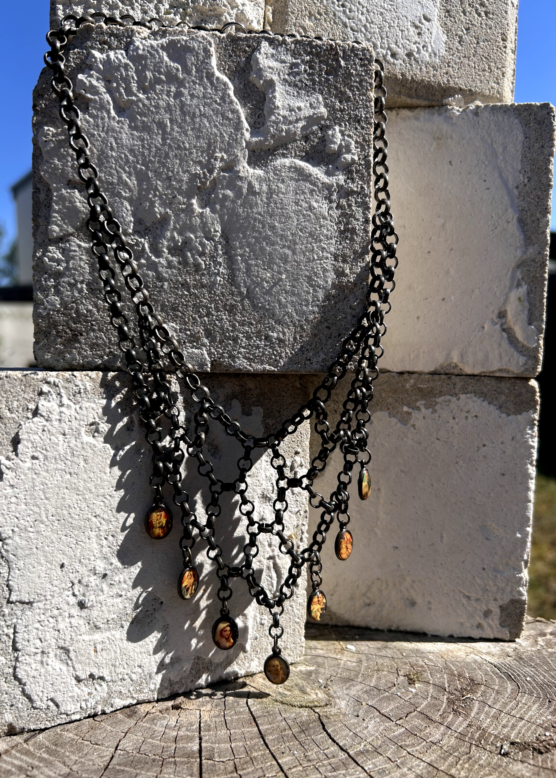 pièce unique, façonnée à partir de bijoux anciens soigneusement sélectionnés, nettoyés et réassemblés pour transmettre un message puissant:

Sept médailles religieuses vintage au fond jauni (Saints, Chérubin, Vierge), serties dans du laiton, issues d’un ancien collier de perles de culture.
Des anneaux en inox, récupérés un à un sur un collier cascade, assemblés pour créer un plastron pyramidal. Vu de face.