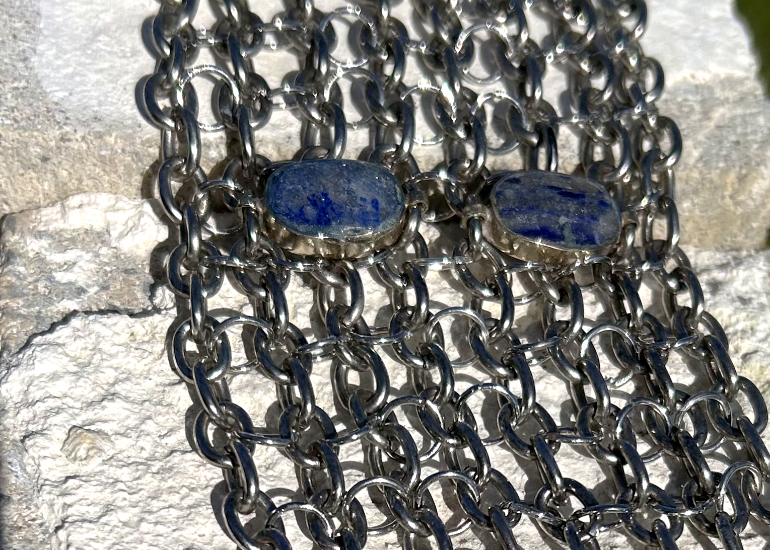 Bracelet de force conçu à partir de mailles récupérées sur deux anciens colliers en cascade, reliées par des anneaux en inox plus fins sur la largeur. Deux pendentifs sertis en pâte de verre bleue, provenant d’un vieux collier d’Essaouira, sont directement attachés aux anneaux du bracelet. Il se ferme grâce à huit crochets à la française, fabriqués à partir de huit maillons de bracelet. Dimensions : 8 cm de hauteur, 18 cm de largeur ; adapté à un poignet de 17 cm de pourtour.