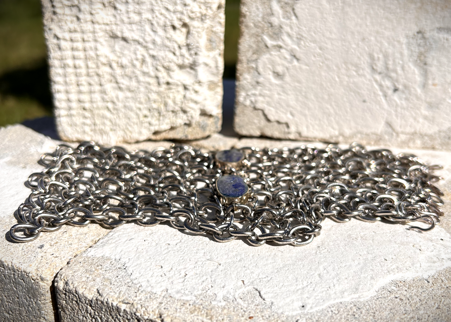 Bracelet de force conçu à partir de mailles récupérées sur deux anciens colliers en cascade, reliées par des anneaux en inox plus fins sur la largeur. Deux pendentifs sertis en pâte de verre bleue, provenant d’un vieux collier d’Essaouira, sont directement attachés aux anneaux du bracelet. Il se ferme grâce à huit crochets à la française, fabriqués à partir de huit maillons de bracelet. Dimensions : 8 cm de hauteur, 18 cm de largeur ; adapté à un poignet de 17 cm de pourtour.