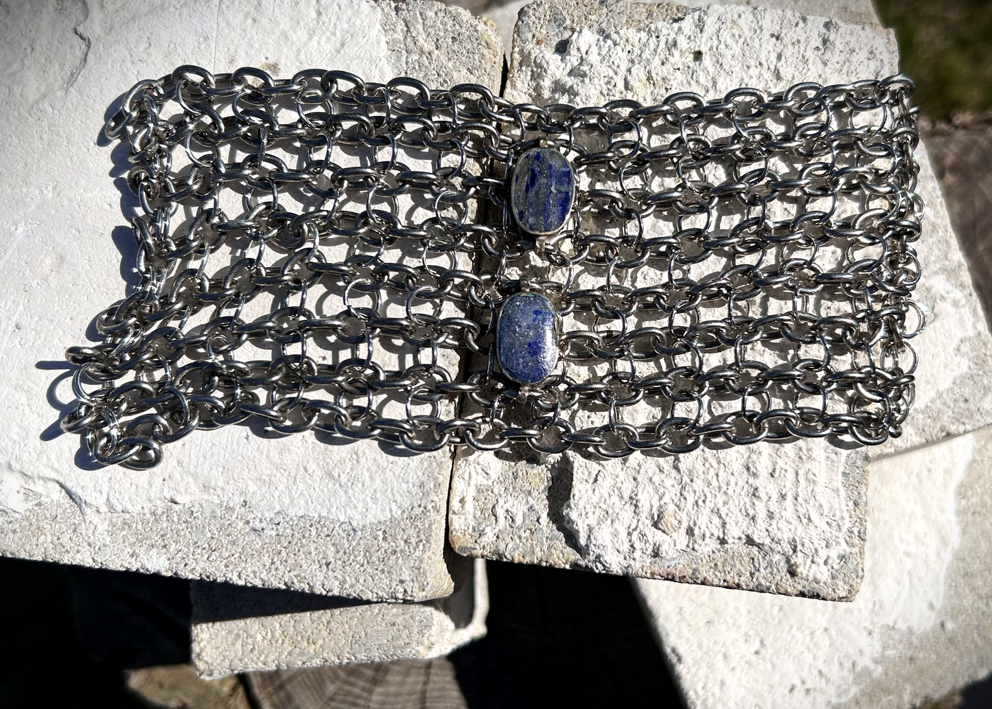 Bracelet de force conçu à partir de mailles récupérées sur deux anciens colliers en cascade, reliées par des anneaux en inox plus fins sur la largeur. Deux pendentifs sertis en pâte de verre bleue, provenant d’un vieux collier d’Essaouira, sont directement attachés aux anneaux du bracelet. Il se ferme grâce à huit crochets à la française, fabriqués à partir de huit maillons de bracelet. Dimensions : 8 cm de hauteur, 18 cm de largeur ; adapté à un poignet de 17 cm de pourtour.