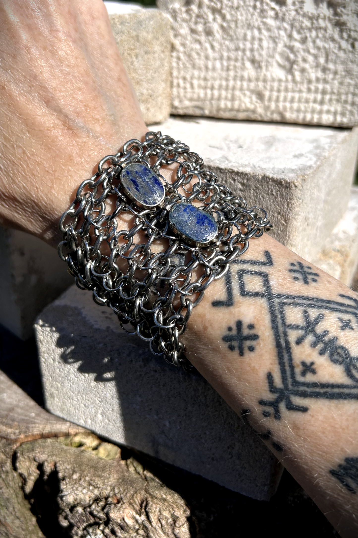 Bracelet de force conçu à partir de mailles récupérées sur deux anciens colliers en cascade, reliées par des anneaux en inox plus fins sur la largeur. Deux pendentifs sertis en pâte de verre bleue, provenant d’un vieux collier d’Essaouira, sont directement attachés aux anneaux du bracelet. Il se ferme grâce à huit crochets à la française, fabriqués à partir de huit maillons de bracelet. Dimensions : 8 cm de hauteur, 18 cm de largeur ; adapté à un poignet de 17 cm de pourtour. Vue portée.