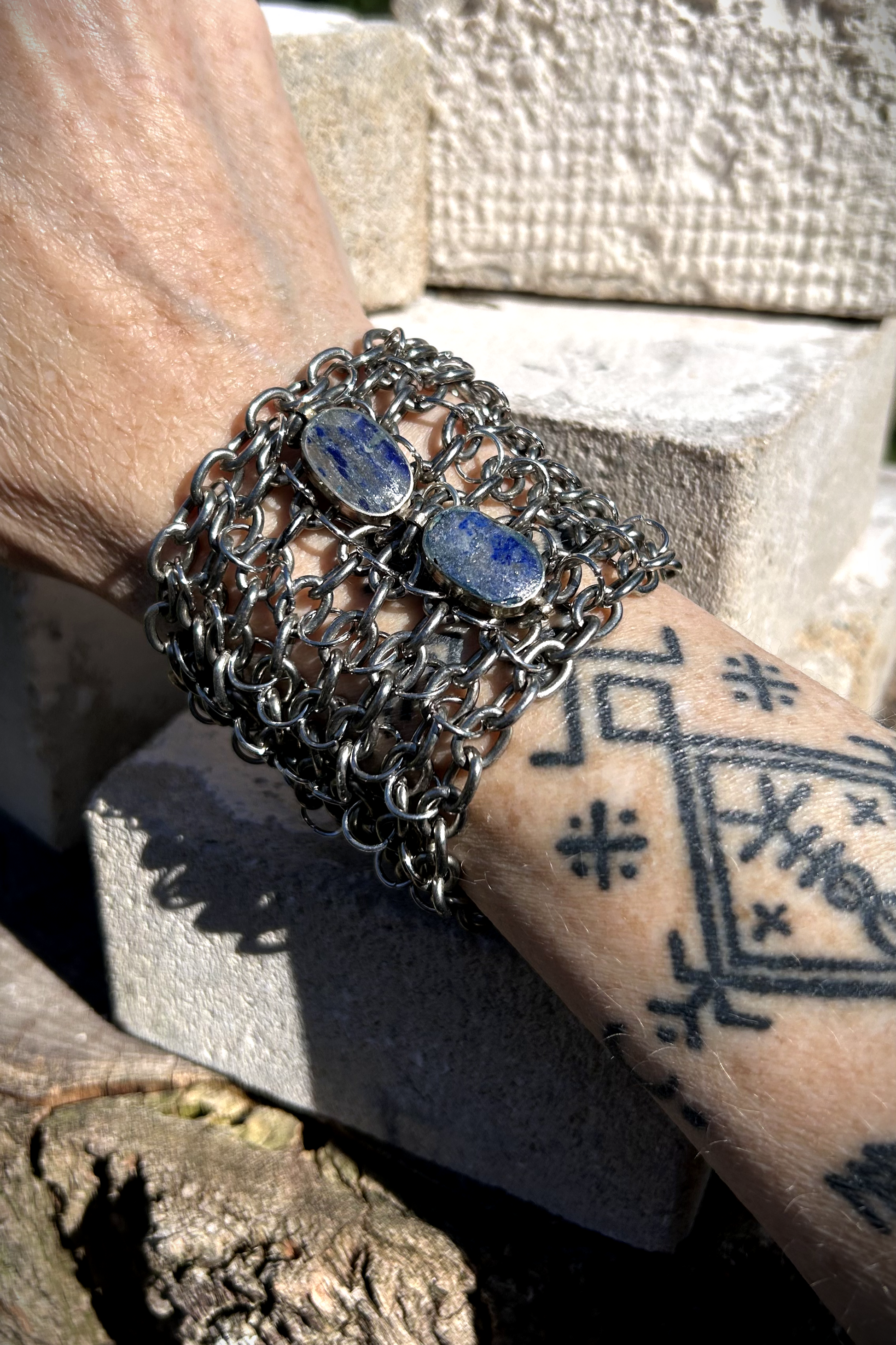 Bracelet de force conçu à partir de mailles récupérées sur deux anciens colliers en cascade, reliées par des anneaux en inox plus fins sur la largeur. Deux pendentifs sertis en pâte de verre bleue, provenant d’un vieux collier d’Essaouira, sont directement attachés aux anneaux du bracelet. Il se ferme grâce à huit crochets à la française, fabriqués à partir de huit maillons de bracelet. Dimensions : 8 cm de hauteur, 18 cm de largeur ; adapté à un poignet de 17 cm de pourtour. Vue portée.