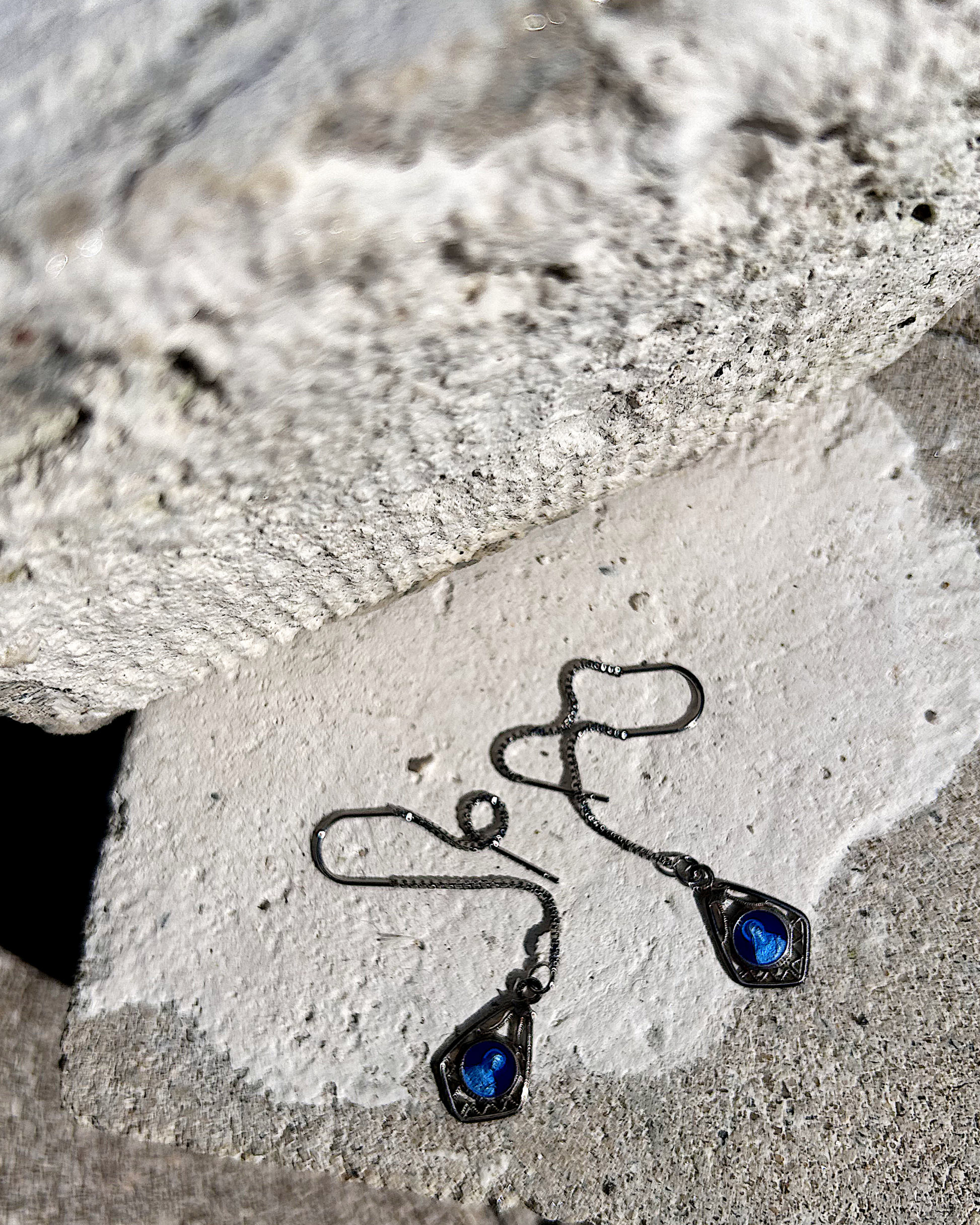 Petites boucles d’oreilles légères, composées d’une chaîne en inox hypoallergénique, suspendue à un U en inox qui traverse le lobe. À son extrémité, une médaille en métal bleu émaillée représentant la Vierge Marie est délicatement accrochée. Vue de dessus.