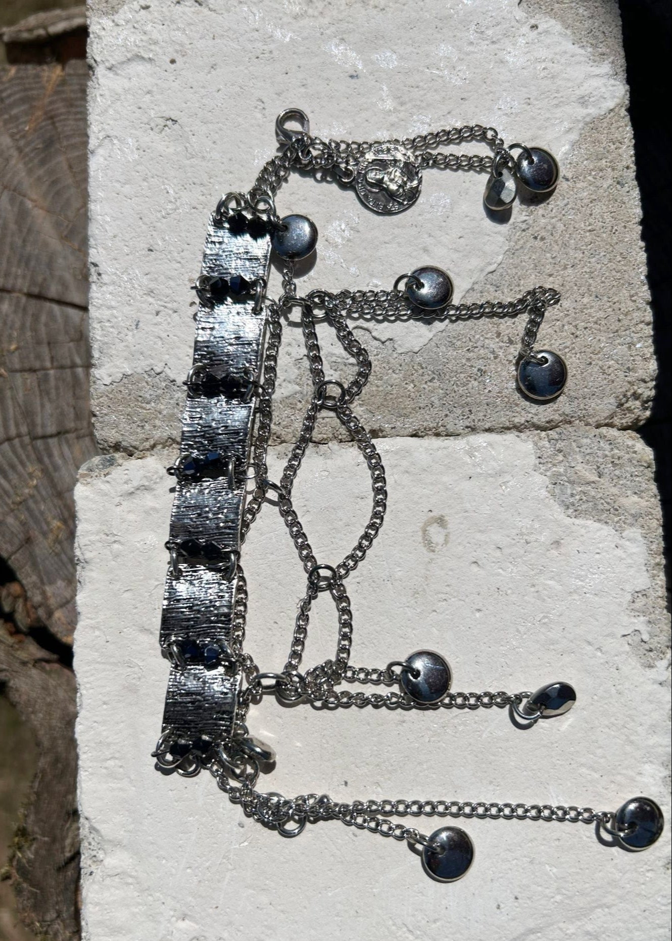 Ce bracelet est une pièce unique, façonnée avec à partir de matériaux chinés : Chainettes et carrés de métal inconnu récupérés sur un collier berbère, brossés puis courbés. Petits maillons en inox  pour alléger l’ensemble. Perles double cône losange noires et bleutés brillantes récupérés, fixés sur tiges en inoxydable. Fermoir menotte. Vue de dessus au soleil.