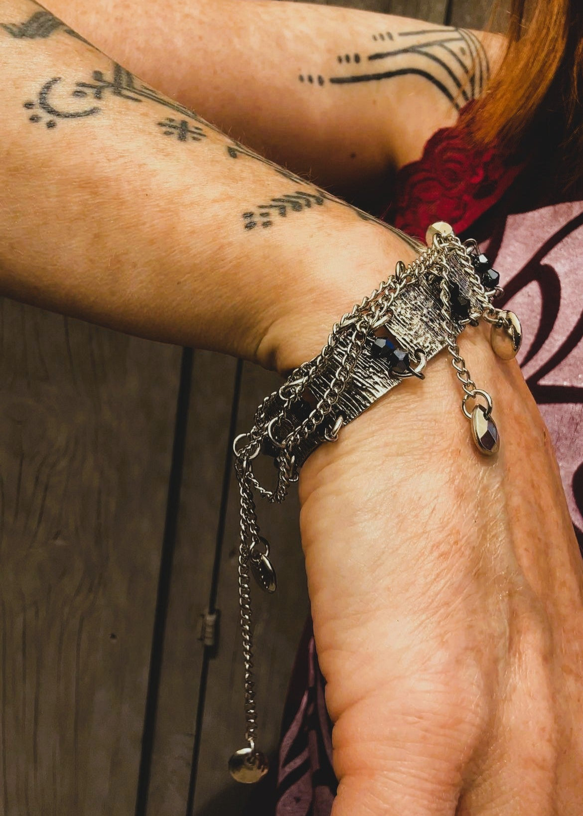 Ce bracelet est une pièce unique, façonnée avec à partir de matériaux chinés : Chainettes et carrés de métal inconnu récupérés sur un collier berbère, brossés puis courbés. Petits maillons en inox  pour alléger l’ensemble. Perles double cône losange noires et bleutés brillantes récupérés, fixés sur tiges en inoxydable. Fermoir menotte. Vue du bracelet porté.