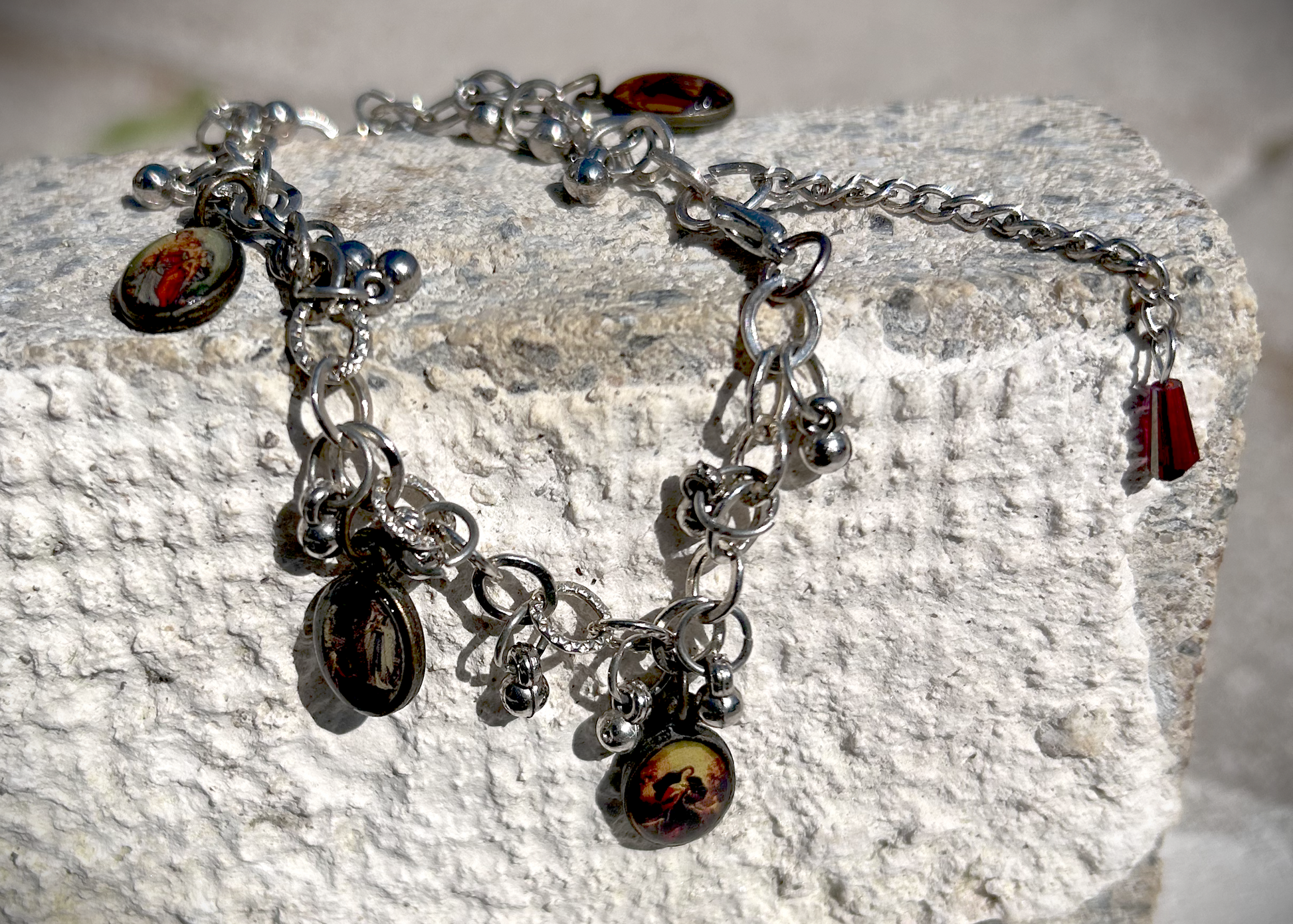 Bracelet recyclé d'un collier, agrémenté de pampilles indiennes, et de médailles religieuses de Saints. J'ai accroché une perle rouge au fermoir, au Japon le rouge protège contre les mauvais esprits et les maladies. Vu du bracelet posé à cheval sur une brique.