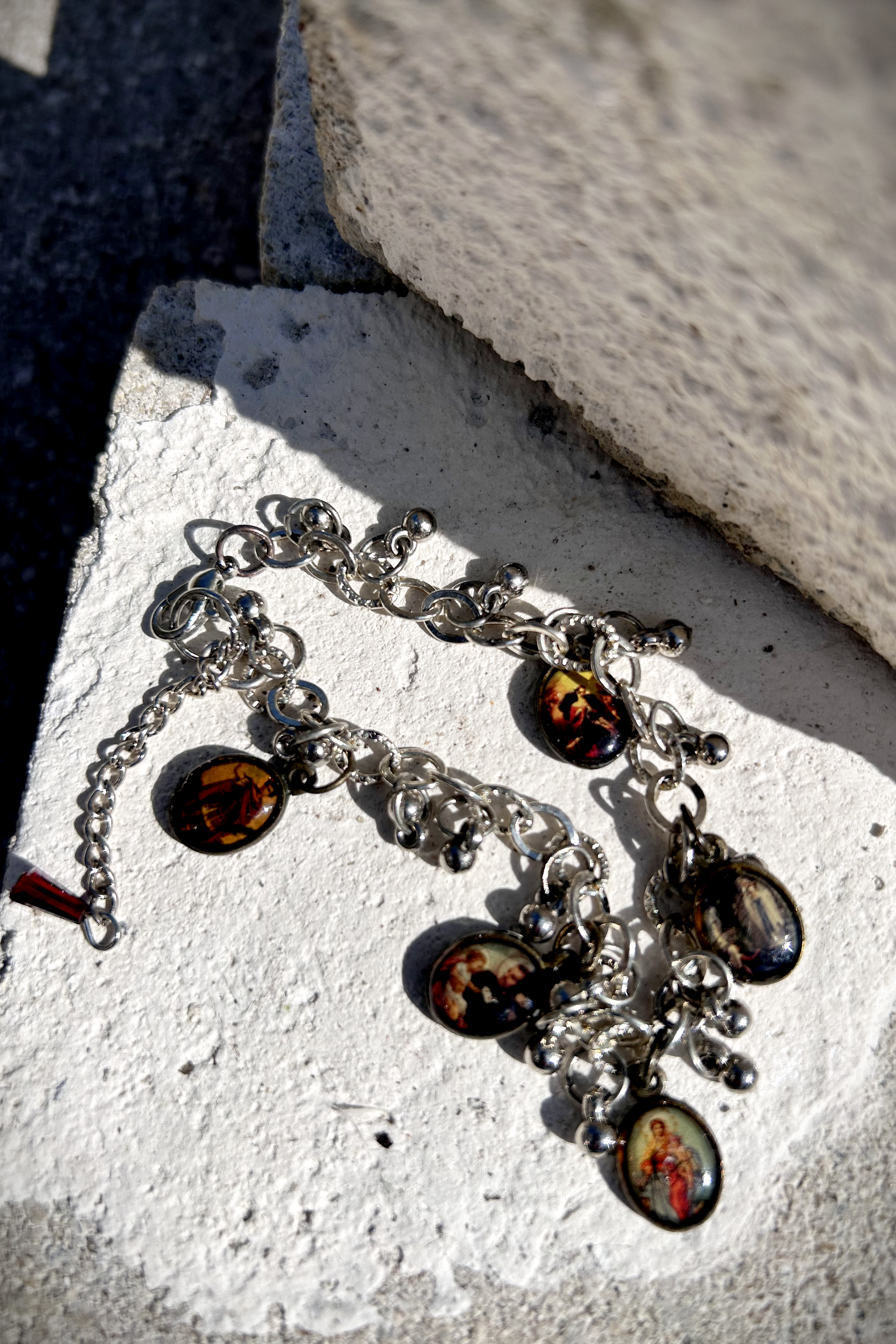 Bracelet recyclé d'un collier, agrémenté de pampilles indiennes, et de médailles religieuses de Saints. J'ai accroché une perle rouge au fermoir, au Japon le rouge protège contre les mauvais esprits et les maladies. Vue de dessus des médailles.