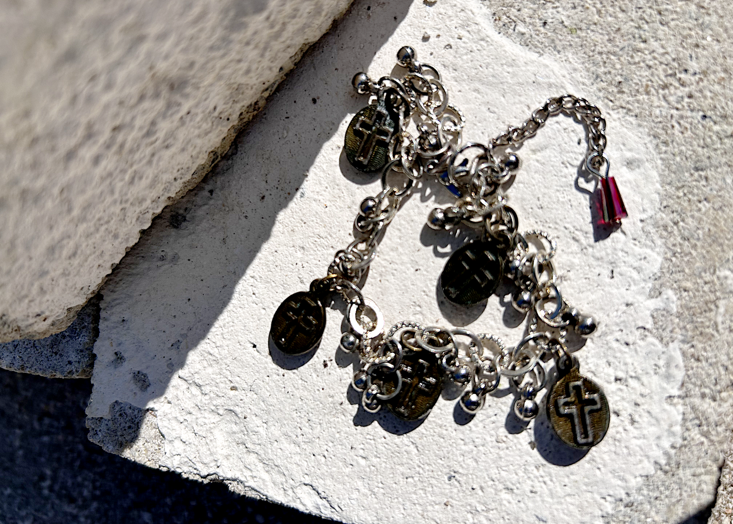 Bracelet recyclé d'un collier, agrémenté de pampilles indiennes, et de médailles religieuses de Saints. J'ai accroché une perle rouge au fermoir, au Japon le rouge protège contre les mauvais esprits et les maladies. Vue du dos des médailles, présentant une croix religieuse.