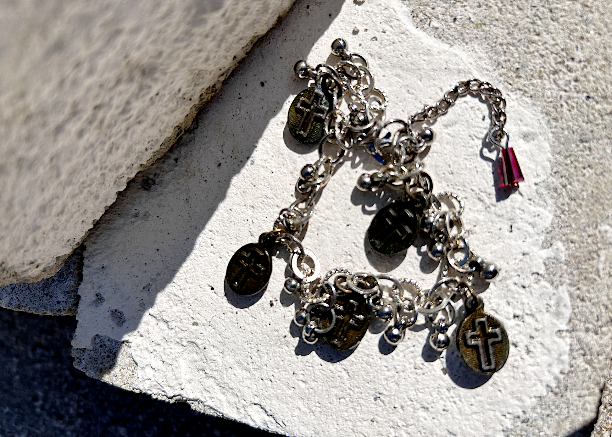 Bracelet recyclé d'un collier, agrémenté de pampilles indiennes, et de médailles religieuses de Saints. J'ai accroché une perle rouge au fermoir, au Japon le rouge protège contre les mauvais esprits et les maladies. Vue du dos des médailles, présentant une croix religieuse.