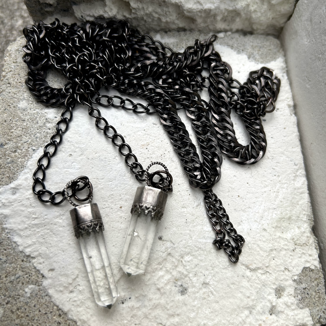 Ce collier se compose de chaînes en acier inoxydable noir, mailles gourmettes, embellies par des pointes de quartz délicatement serties en argent 950 poinçonné. Conçu pour être enroulé élégamment autour du cou. Un petit maillon central installé permet de faire passé en son sein les deux extrémités de ce fil pour un rendu élégant.