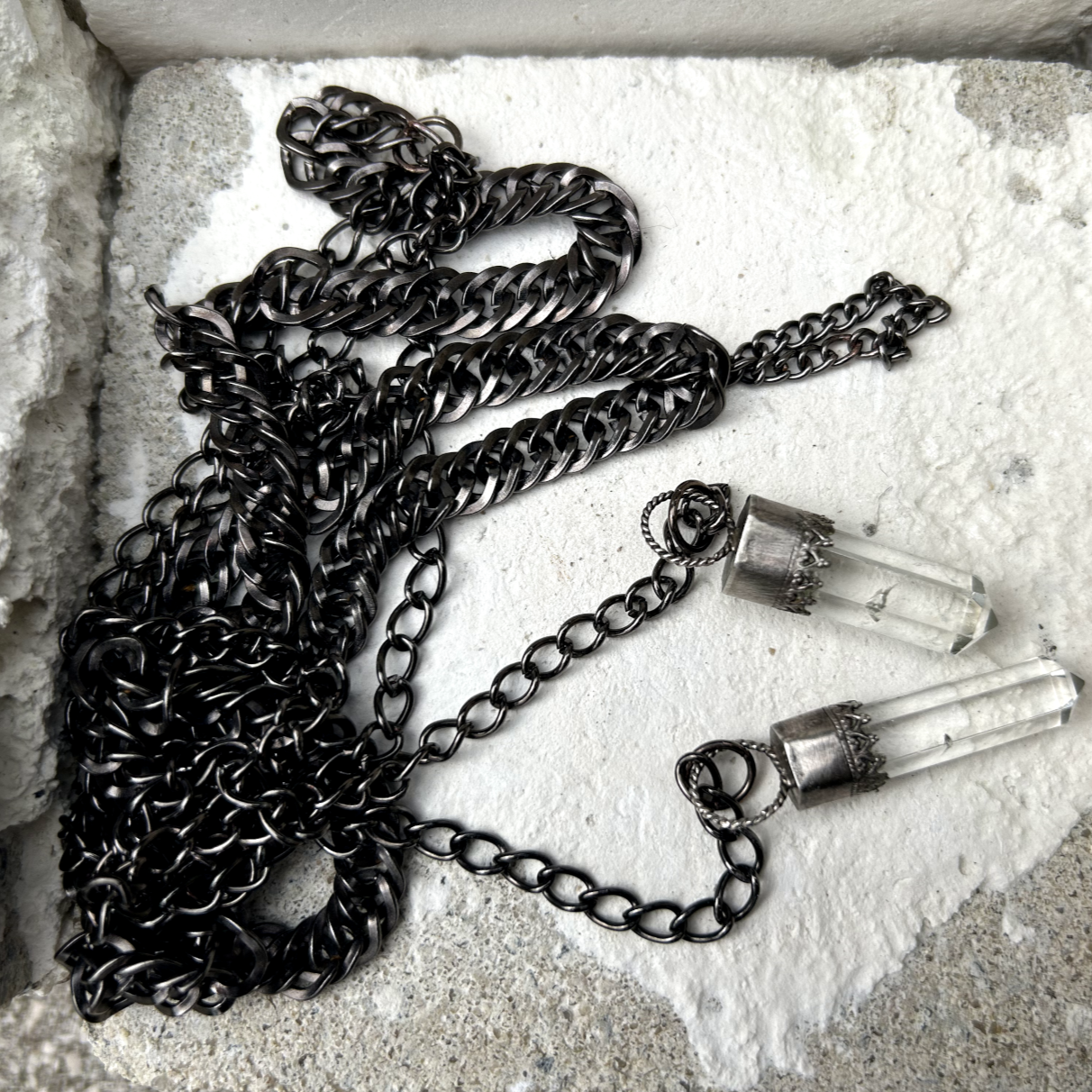 Ce collier se compose de chaînes en acier inoxydable noir, mailles gourmettes, embellies par des pointes de quartz délicatement serties en argent 950 poinçonné. Conçu pour être enroulé élégamment autour du cou. Un petit maillon central installé permet de faire passé en son sein les deux extrémités de ce fil pour un rendu élégant.