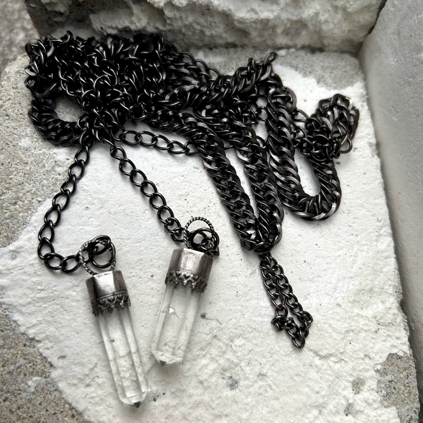 Ce collier se compose de chaînes en acier inoxydable noir, mailles gourmettes, embellies par des pointes de quartz délicatement serties en argent 950 poinçonné. Conçu pour être enroulé élégamment autour du cou. Un petit maillon central installé permet de faire passé en son sein les deux extrémités de ce fil pour un rendu élégant.