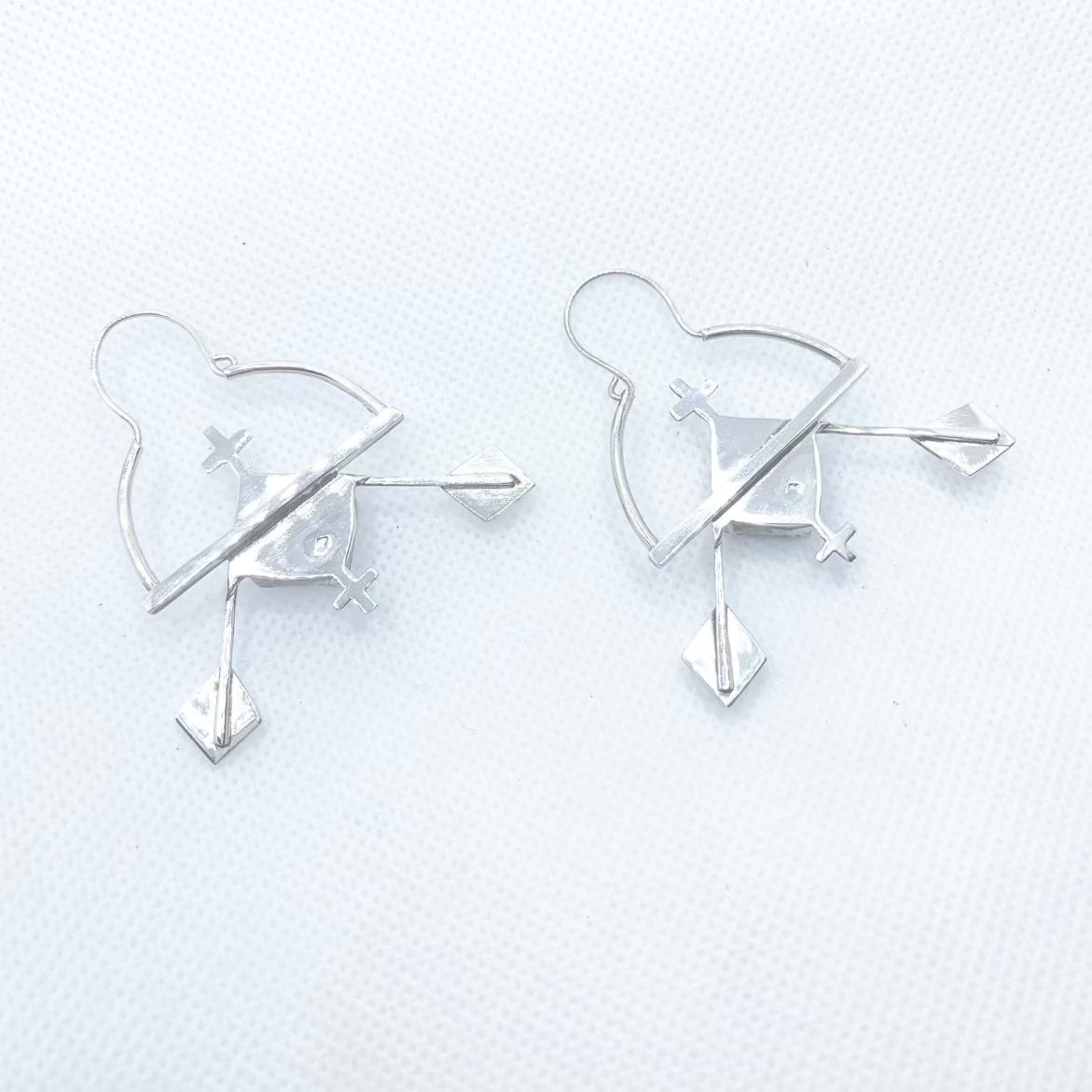 Boucles d'oreilles en argent composées d'une demi-créole en bas de laquelle est soudée une barre. Ici se trouve soudé un serti clos en argent avec une céramique raku bleue irisée carrée, encadré de croix berbères en argent. Le long des cotés du sertis sont soudés deux tiges fines en argent, où s'accrochent les deux losanges de la féminité berbères, cet ensemble symbolisant des rames au soleil couchant. Attaches au centre des demi créoles, crochets s'insérant dans le tube de cette créole. Vue posées de dos. 