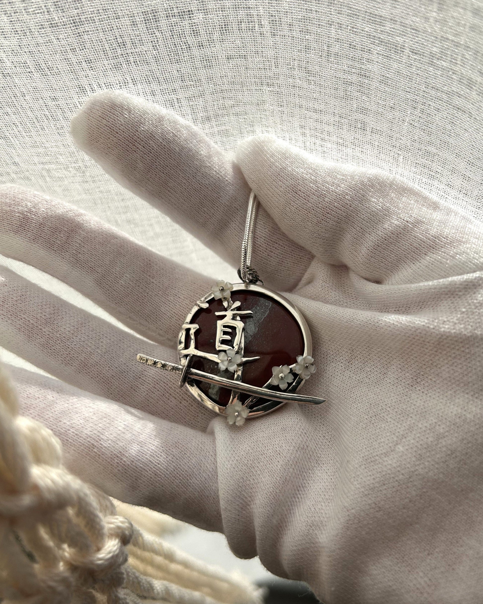pendentif en argent portant le Do du chemin, le sabre de l'iaido et les fleurs de sakura en nacre. Vue de dessus.