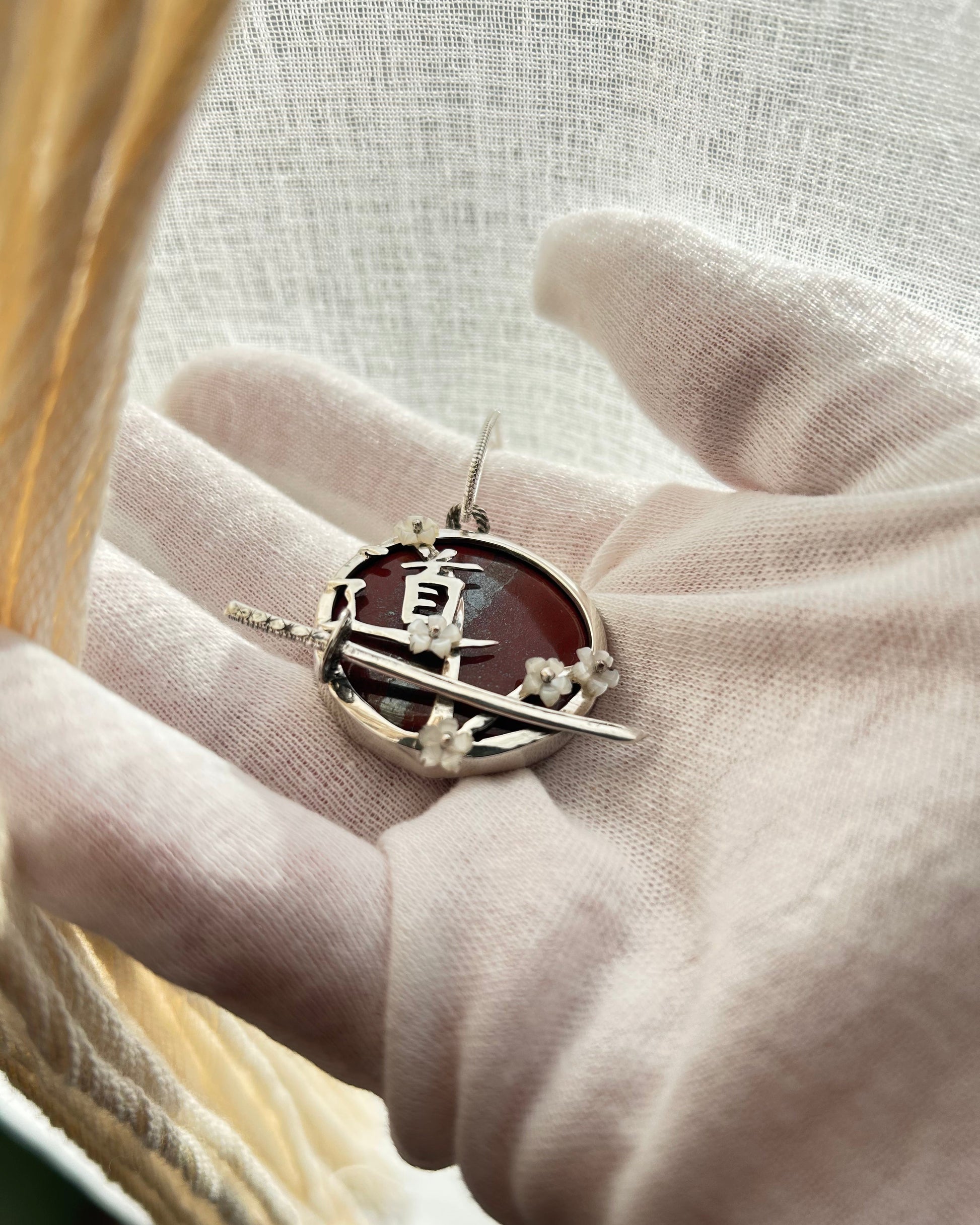 pendentif en argent portant le Do du chemin, le sabre de l'iaido et les fleurs de sakura en nacre. Vue de  3/4 avec sabre en relief et fleurs en nacre rivetées.