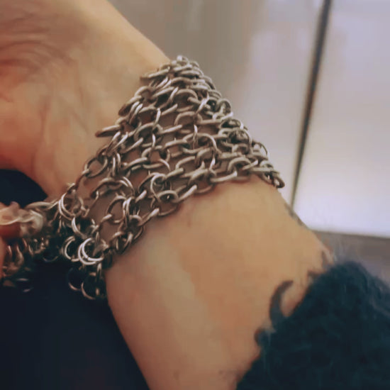 Bracelet de force conçu à partir de mailles récupérées sur deux anciens colliers en cascade, reliées par des anneaux en inox plus fins sur la largeur. Deux pendentifs sertis en pâte de verre bleue, provenant d’un vieux collier d’Essaouira, sont directement attachés aux anneaux du bracelet. Il se ferme grâce à huit crochets à la française, fabriqués à partir de huit maillons de bracelet. Dimensions : 8 cm de hauteur, 18 cm de largeur ; adapté à un poignet de 17 cm de pourtour. Vidéo présentation des attaches