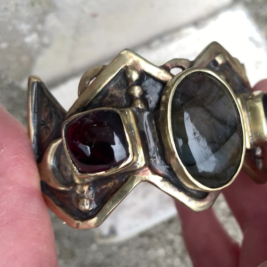 Bracelet de fonte en laiton, sertis d'une labradorite et de deux grenats. Le haut est découpé en W, symbole berbère de la fourdre, et le bas en M (symbole de fécondité). Vidéo de présentation.